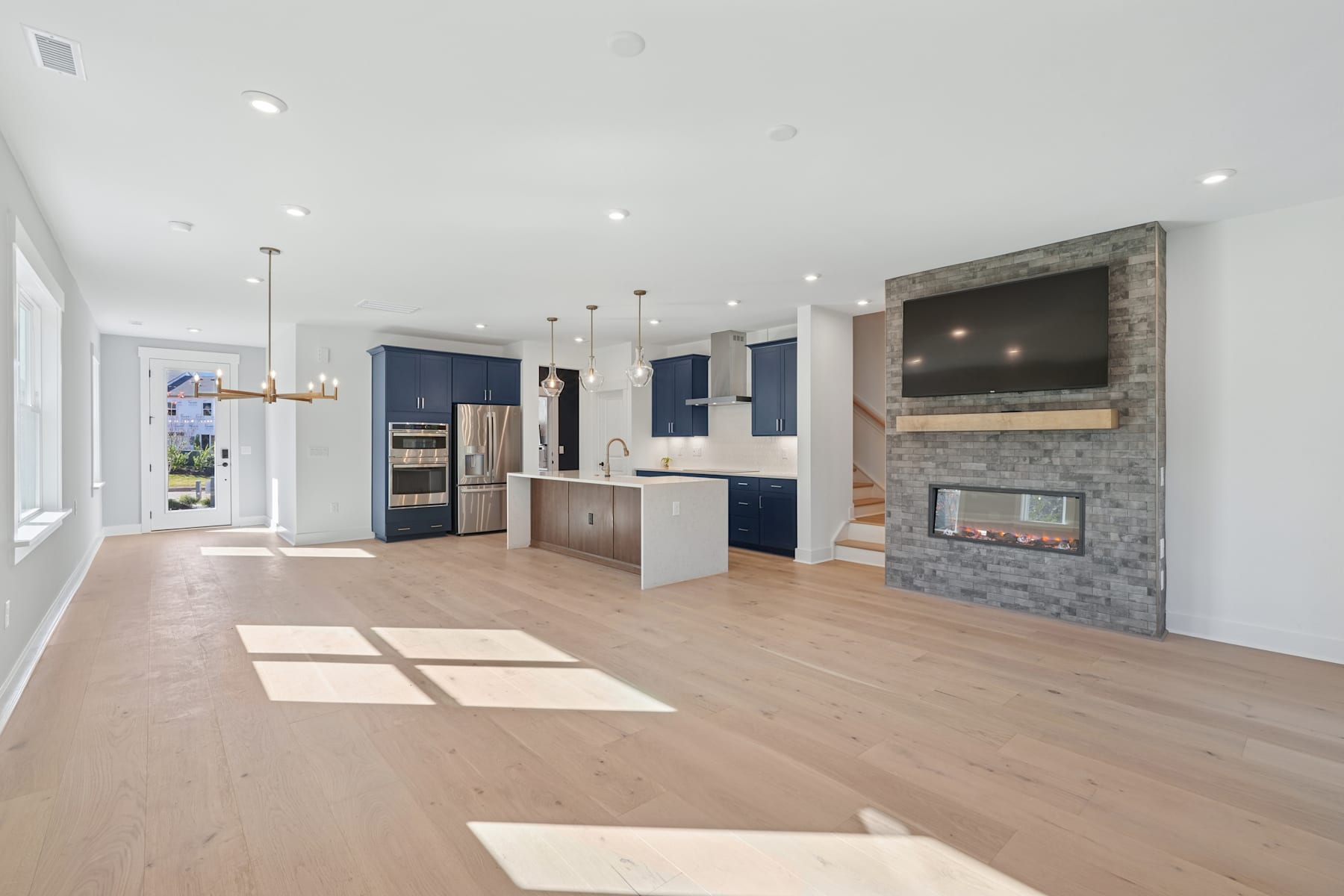 A spacious and modern open-concept living area with a kitchen, fireplace, and hardwood flooring, bathed in natural light from the windows.