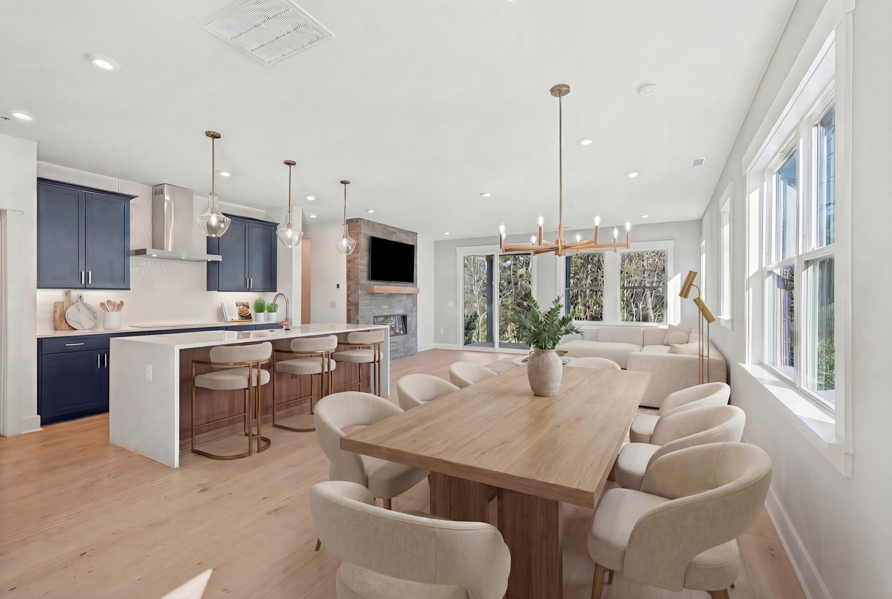 A modern and spacious open-plan kitchen and dining area with a wooden dining table, comfortable upholstered chairs, and a sleek kitchen with dark cabinets and pendant lighting.