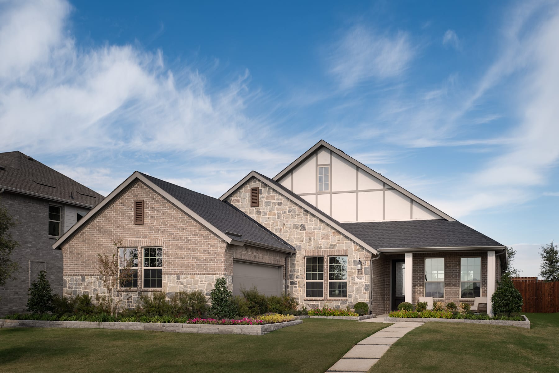 A two-story brick house with a gabled roof and a well-manicured lawn in the foreground, set against a blue sky with wispy clouds.