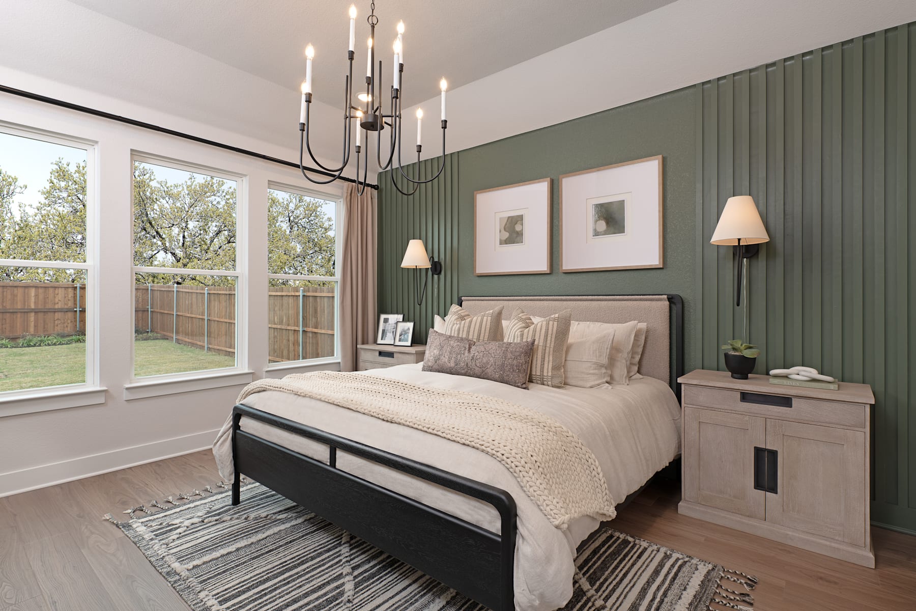 A cozy and inviting bedroom with a large bed, neutral-toned bedding, and a chandelier overhead, set against a backdrop of green-painted walls and large windows overlooking a lush outdoor scene.