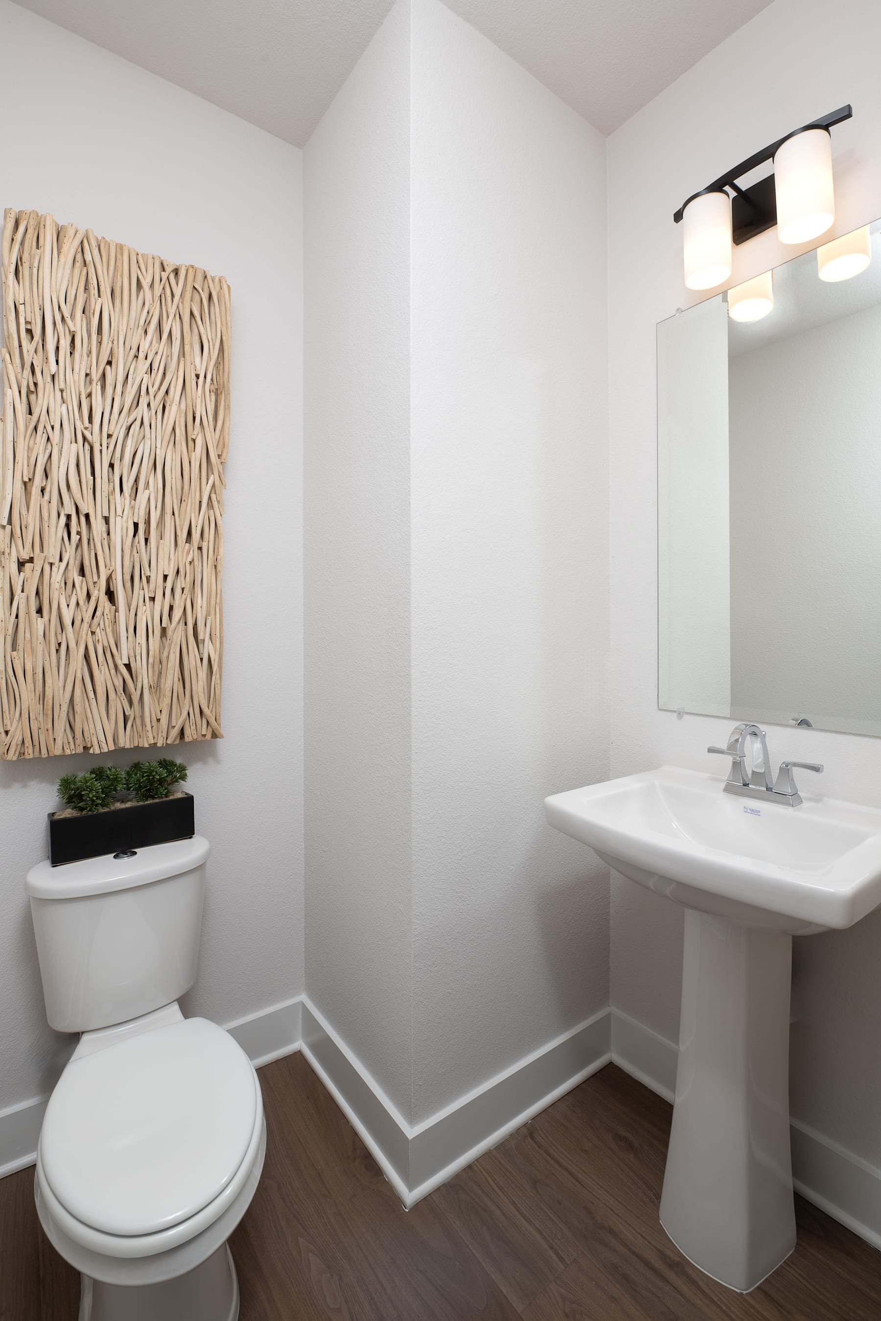 A modern and minimalist bathroom with a white toilet, pedestal sink, and a decorative wooden wall hanging.