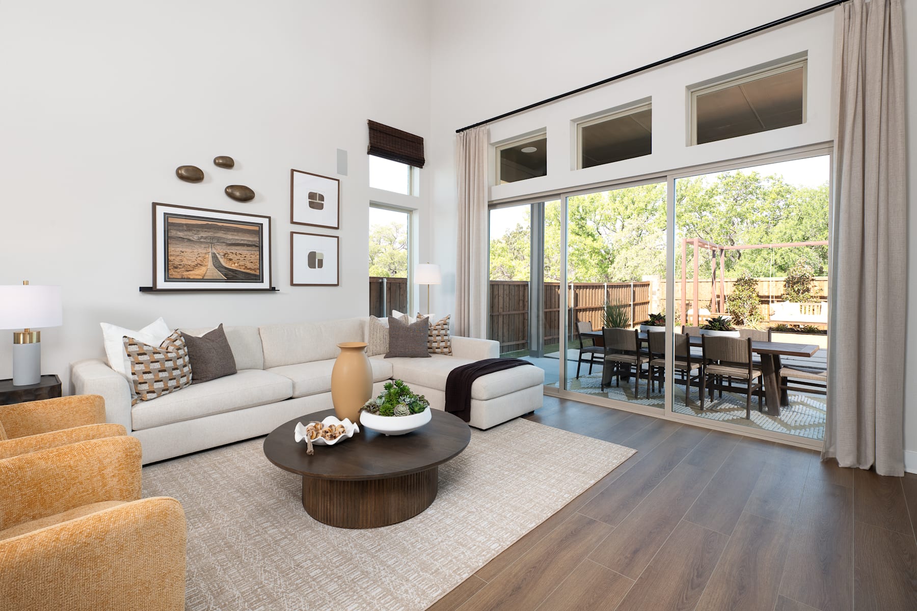 A cozy and modern living room with a plush sofa, a round wooden coffee table, and large windows overlooking a lush outdoor area.