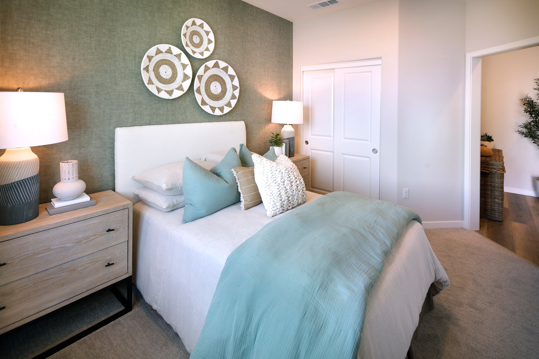 A cozy and inviting bedroom with a white bed, gray and blue bedding, and decorative wall hangings, creating a serene and calming atmosphere.