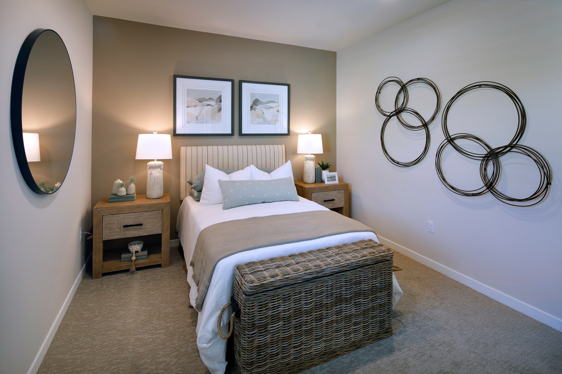 A cozy and inviting bedroom with a neutral color scheme, featuring a bed with a white comforter, a round mirror, and an array of decorative wall art.