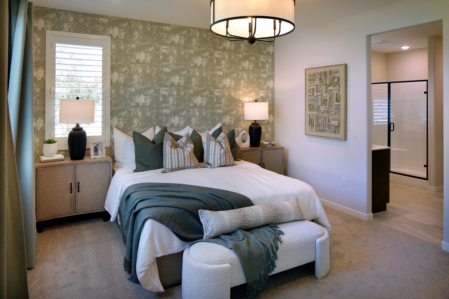A cozy and inviting bedroom with a plush bed, decorative pillows, and a stylish light fixture, set against a textured accent wall and complemented by a modern dresser and artwork.