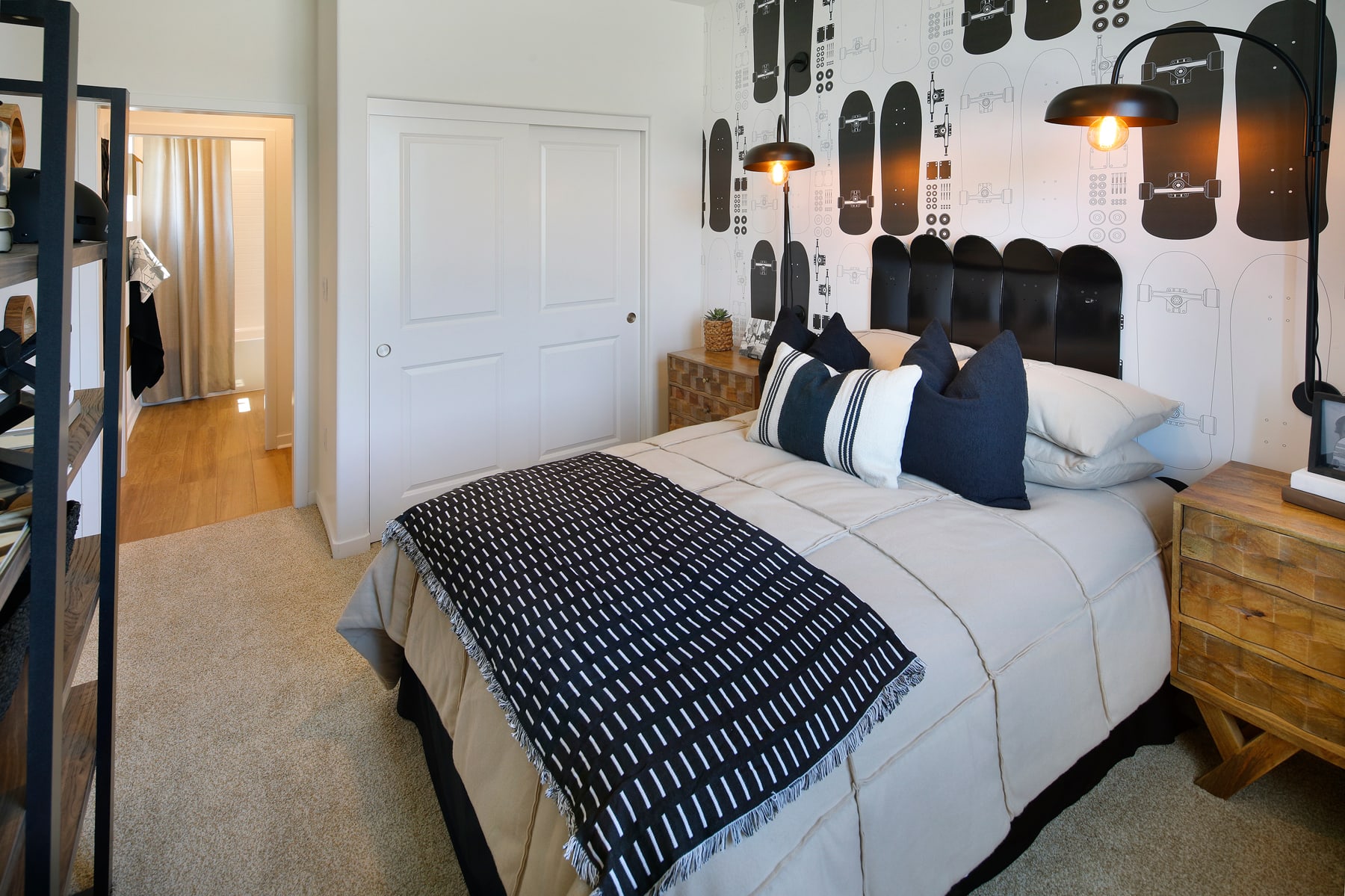 A cozy bedroom with a patterned bedspread, decorative pillows, and a wall adorned with various framed artwork.