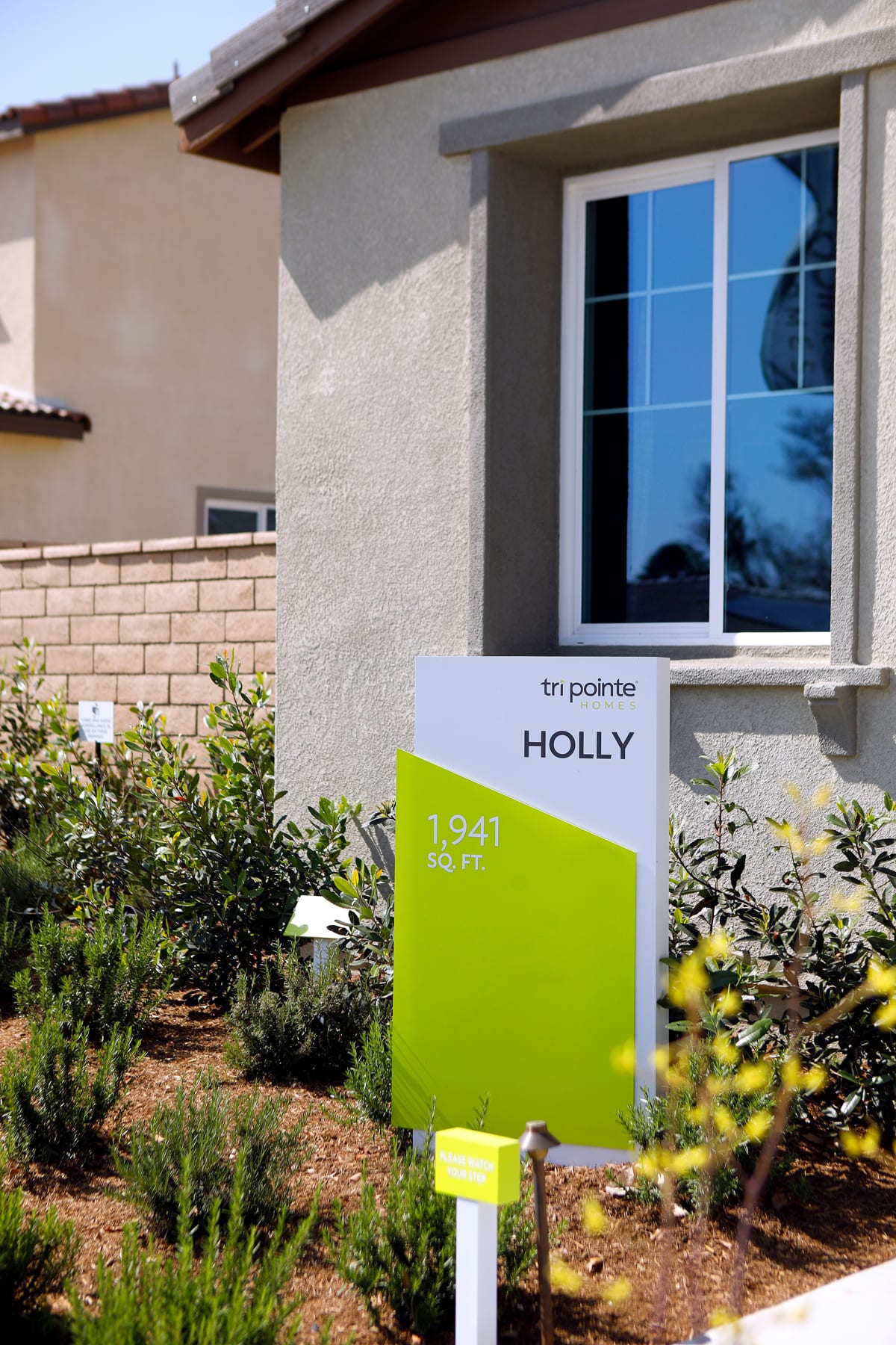A residential building with a green sign displaying the name "Holly" in the foreground, surrounded by landscaping and a clear blue sky in the background.