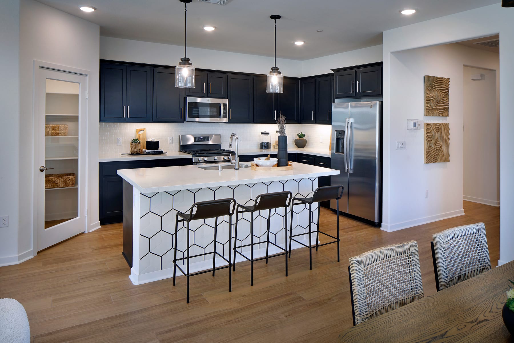 A modern and stylish kitchen with dark cabinets, a white island with a geometric pattern, and pendant lights hanging above the island.