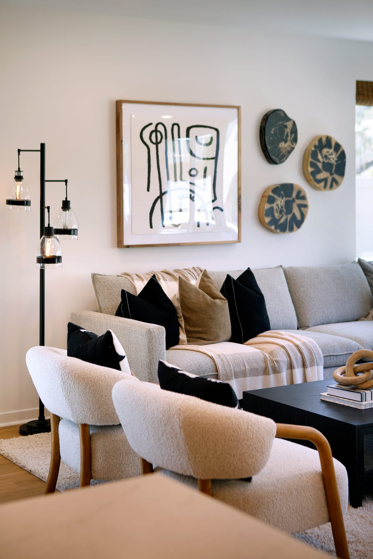 A cozy living room with a gray sectional sofa, wooden accents, and abstract artwork on the wall, complemented by decorative ceramic plates.