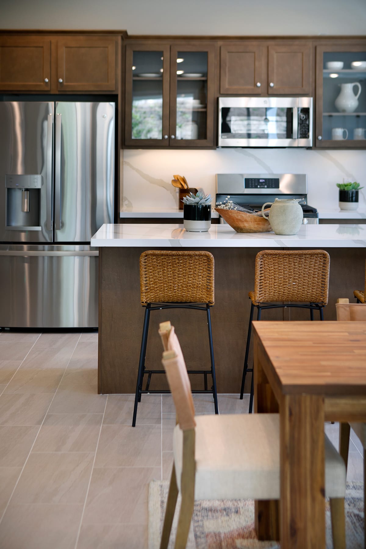 A modern kitchen with wooden cabinets, stainless steel appliances, and wicker stools surrounding a wooden dining table.