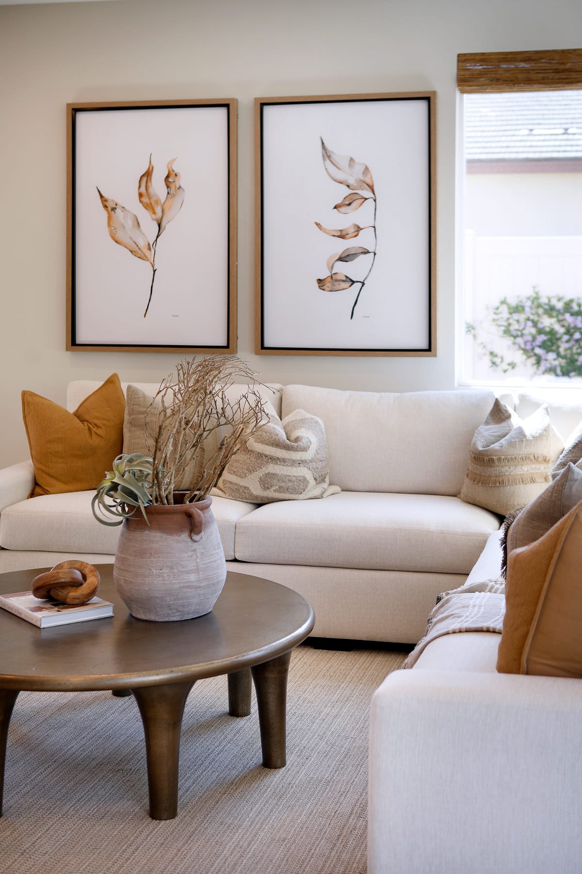 The image depicts a cozy and inviting living room space with a white sofa, a round wooden coffee table, and two framed abstract artworks on the wall. The room is accented with warm tones and natural elements, creating a serene and harmonious atmosphere.