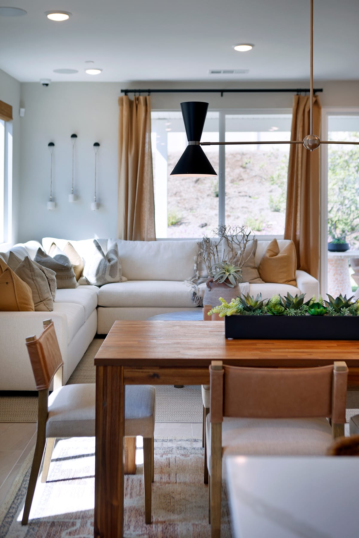 A modern and cozy living room with a large sectional sofa, a wooden dining table, and a large window overlooking the outdoor scenery.