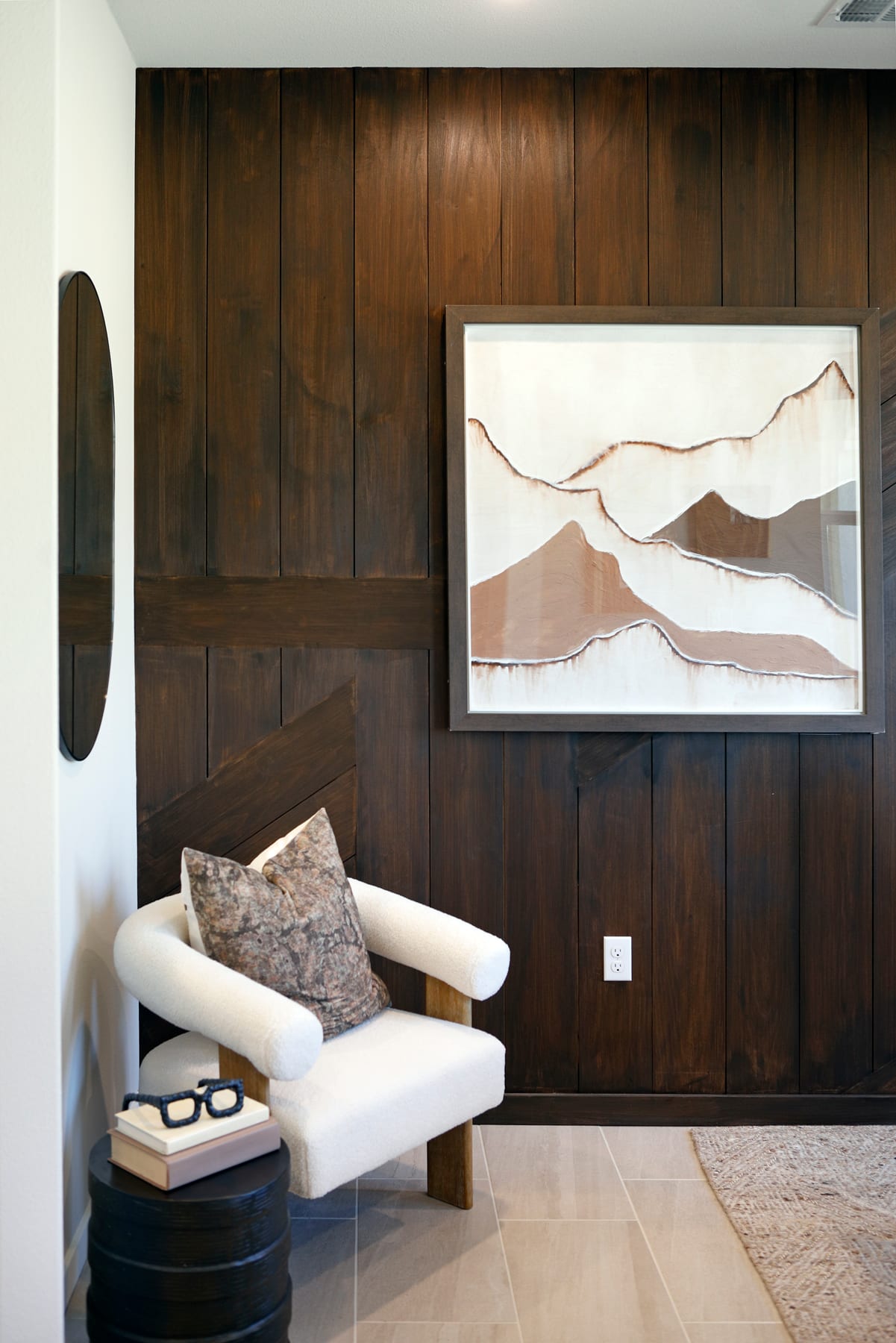 A cozy living room with a wooden accent wall, a white armchair, and a framed abstract landscape painting on the wall.
