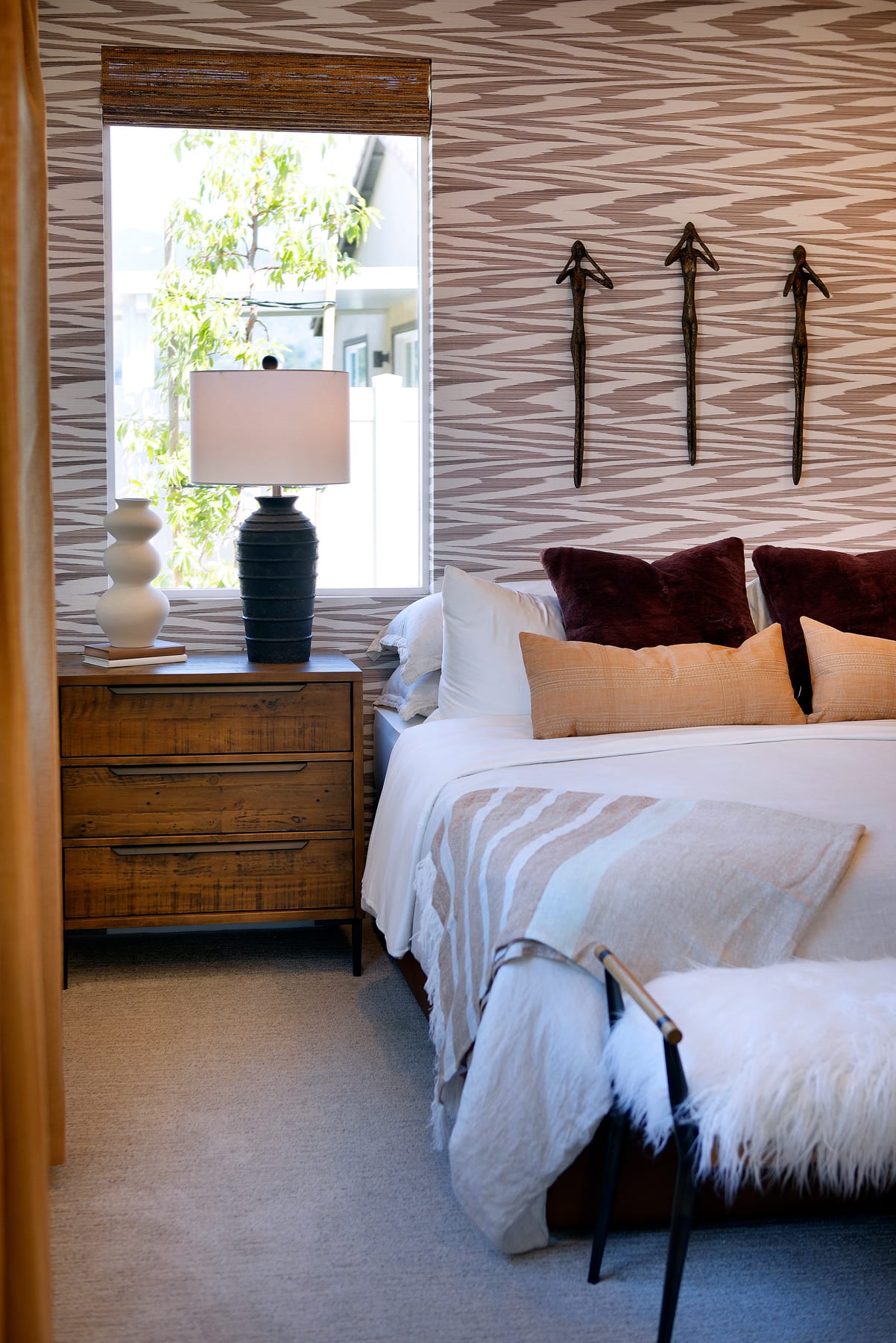 A cozy and inviting bedroom with a wooden dresser, a lamp, and decorative arrows on the wall, overlooking a lush outdoor scene through a window.