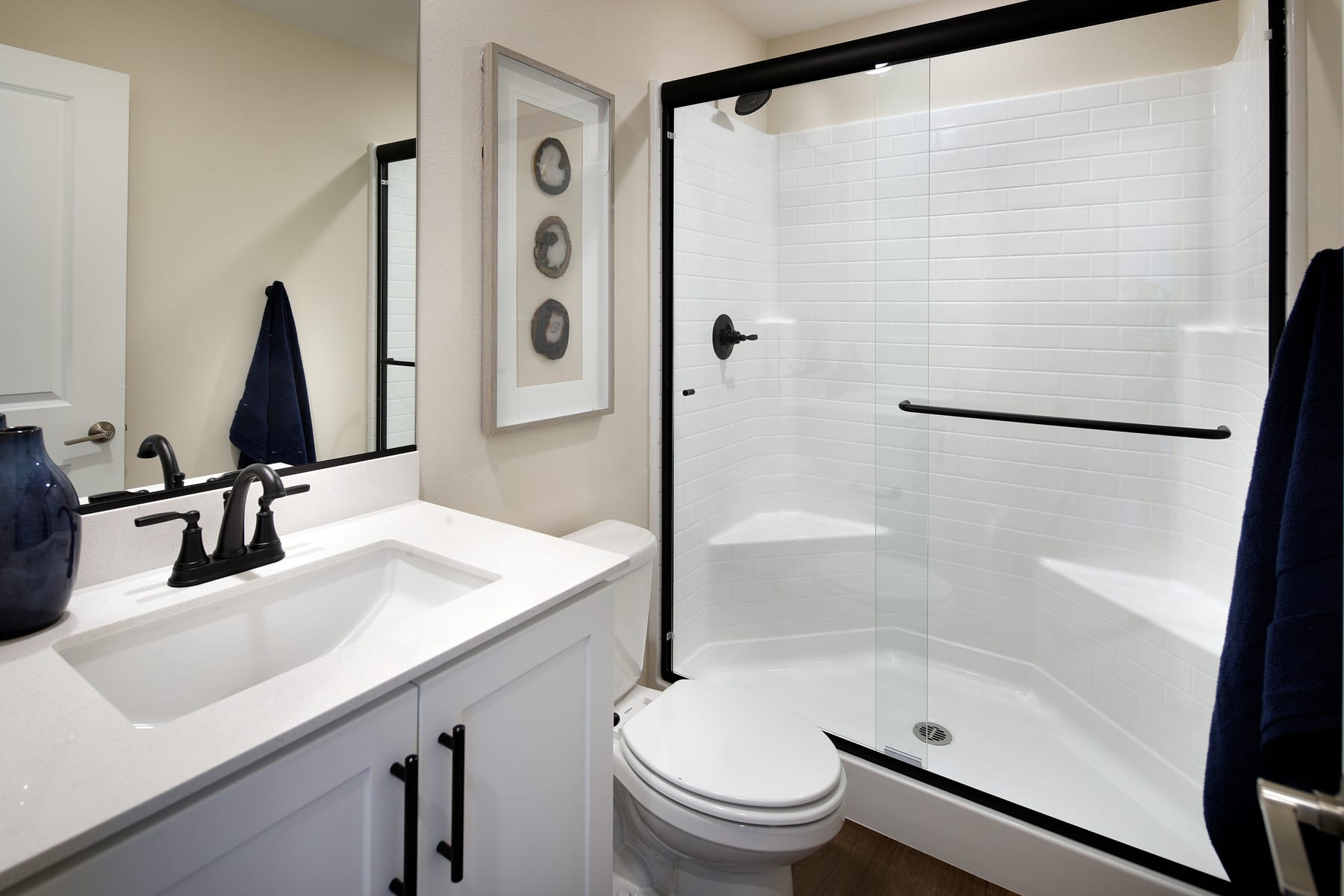A modern bathroom with a white vanity, a framed artwork on the wall, and a glass-enclosed shower enclosure.