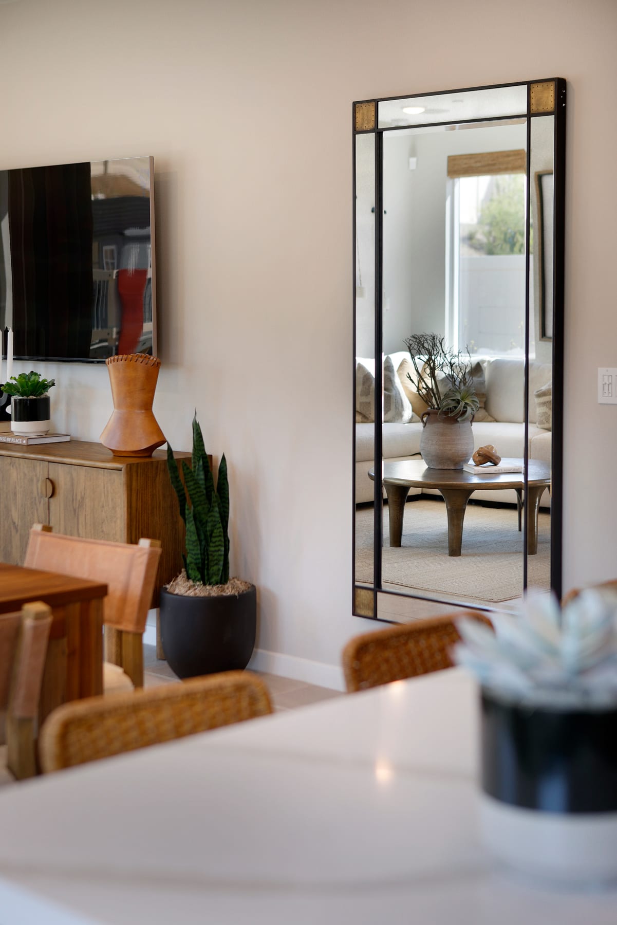 A cozy and well-decorated living room with a large mirror, wooden furniture, and various decorative elements, including plants and a vase with flowers, creating a warm and inviting atmosphere.