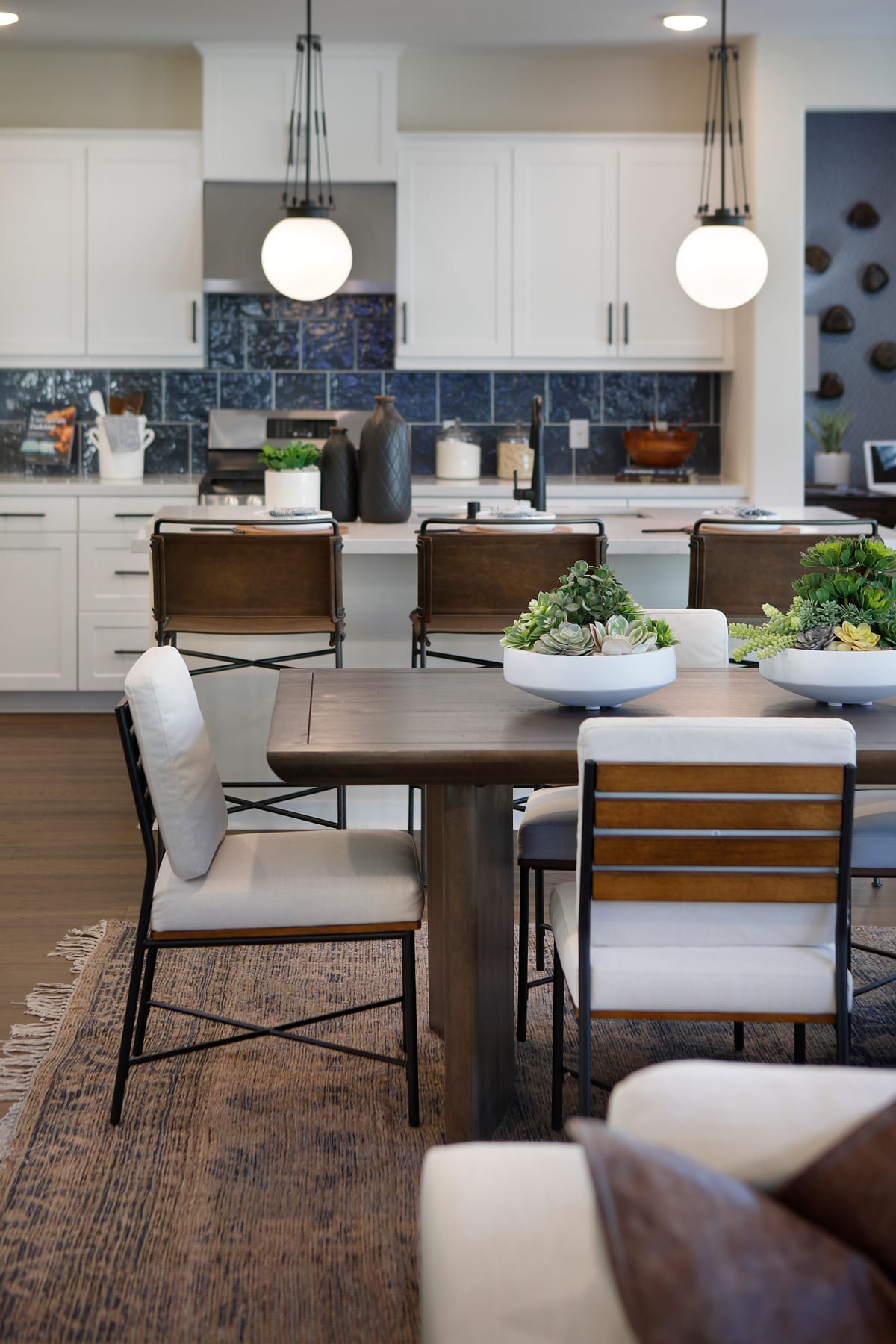 A modern and spacious kitchen with a large wooden dining table, comfortable chairs, and various decorative elements, including a chalkboard wall and pendant lighting fixtures.