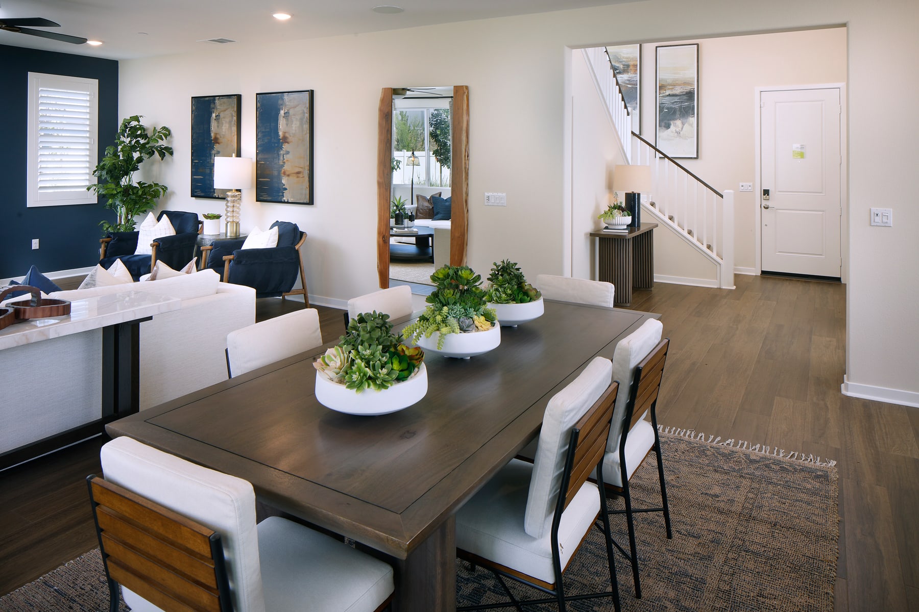 A modern and stylish dining room with a wooden table, white chairs, and various decorative elements such as plants and mirrors adorning the walls.