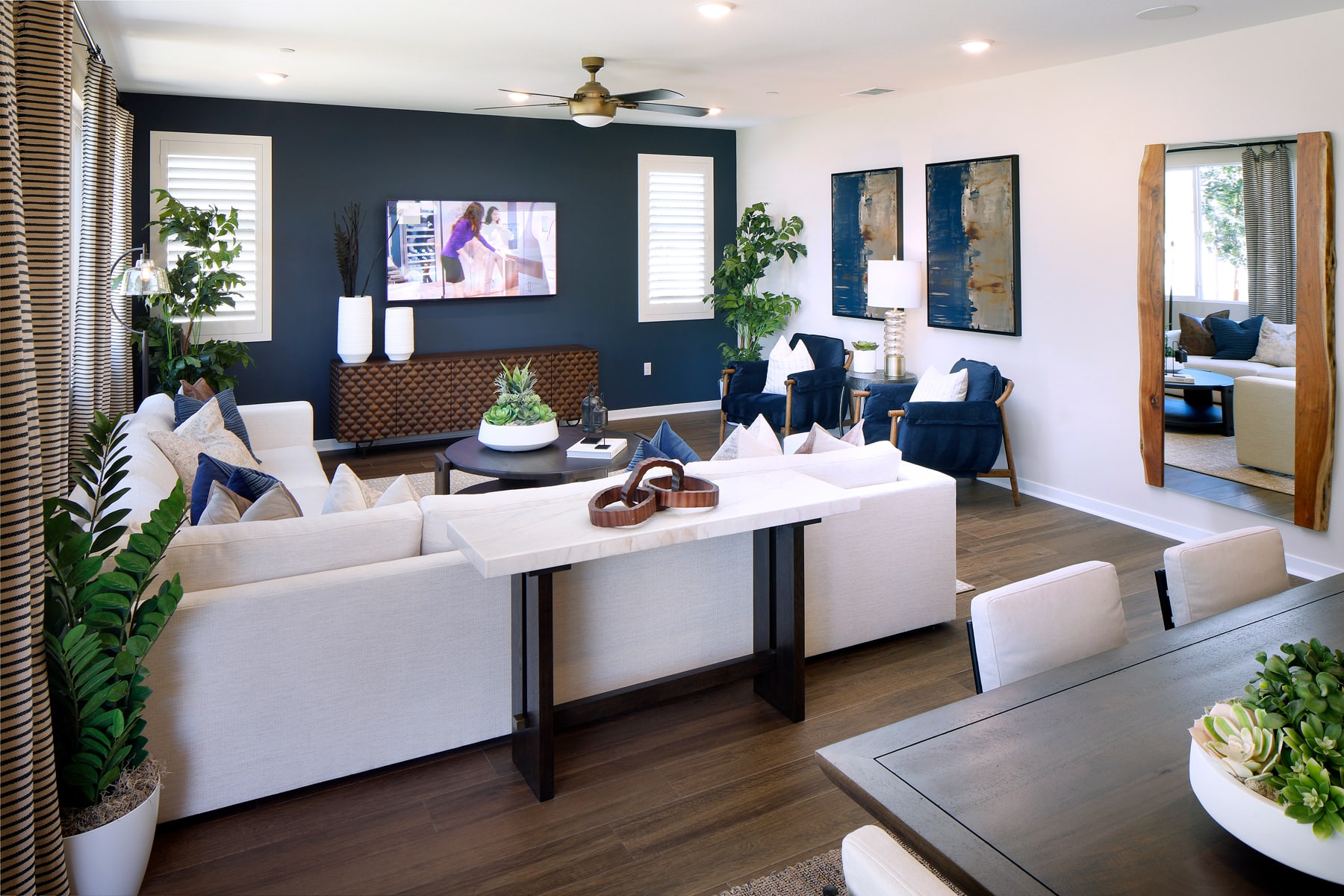 A modern and stylish living room with white furniture, dark accent walls, and various decorative elements such as plants and artwork.