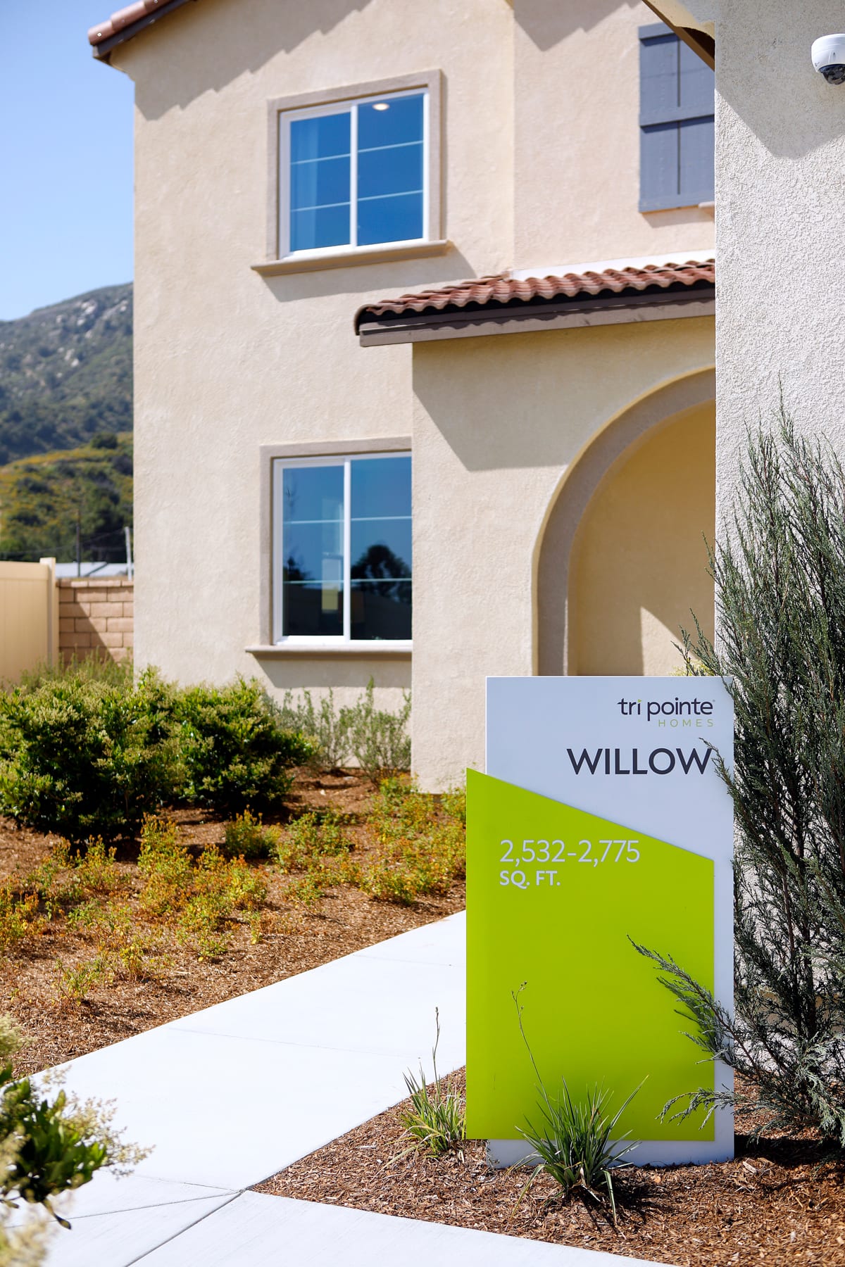 A two-story stucco house with a tiled roof and large windows, surrounded by landscaping and a sign advertising the "Willow" property.