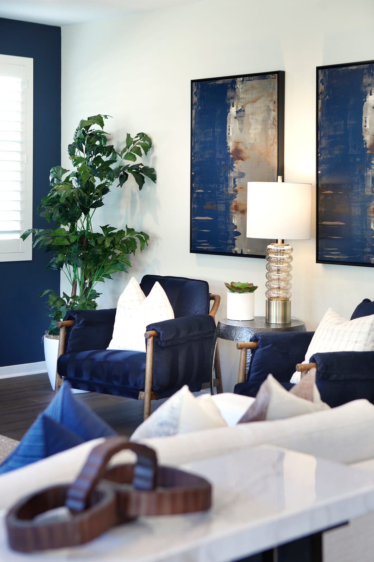 A cozy living room with plush navy blue sofas, abstract art on the walls, and a potted plant adding a touch of greenery to the space.