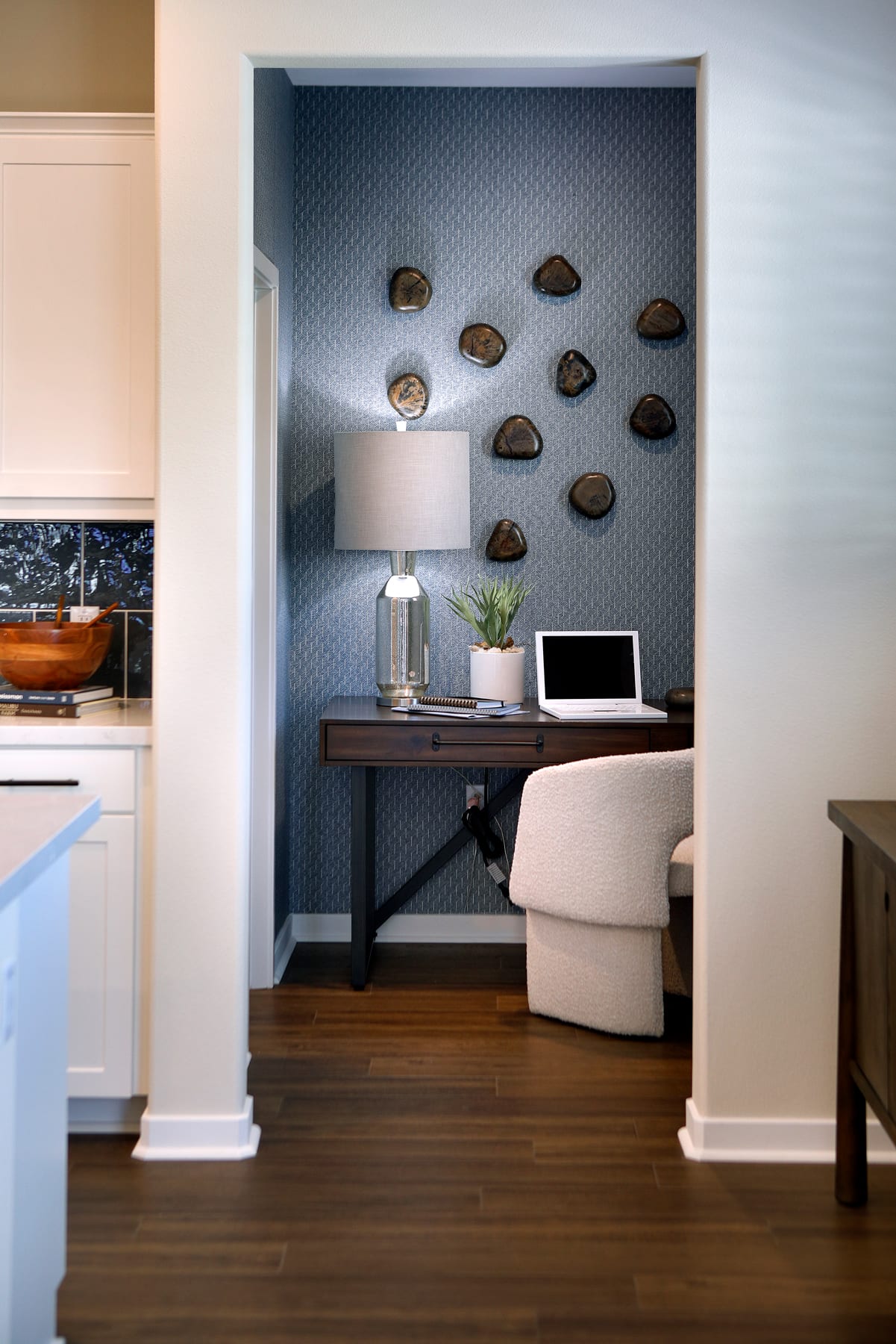 A cozy home office nook with a wooden desk, a lamp, and a potted plant, set against a wall adorned with decorative rock formations.