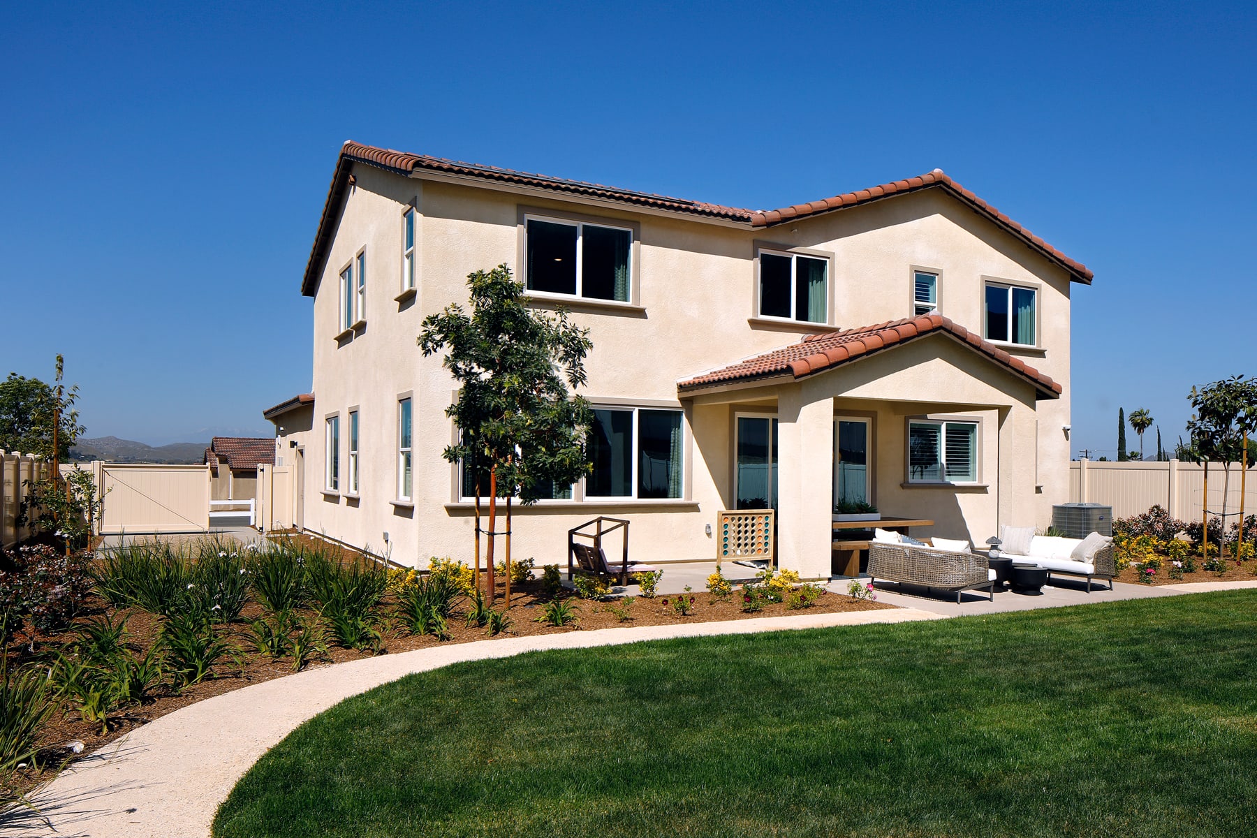 A two-story residential house with a tiled roof, surrounded by a well-maintained lawn and landscaping, set against a clear blue sky.