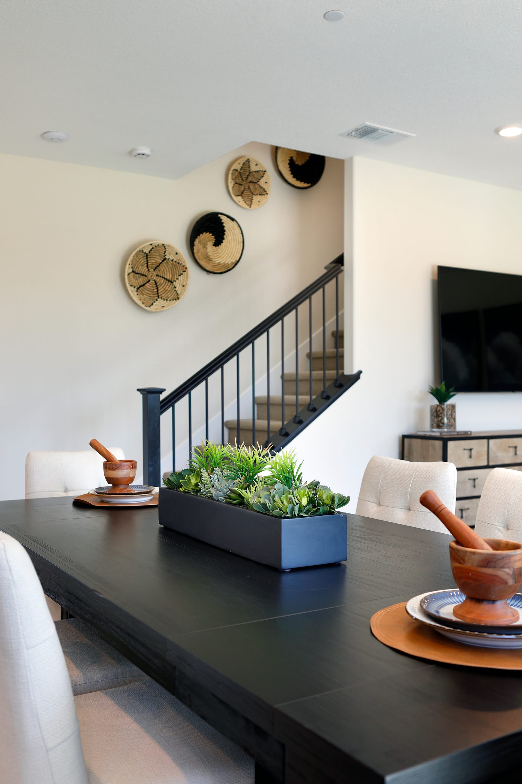A modern and minimalist dining area with a large wooden table, potted plants, and decorative wall art.
