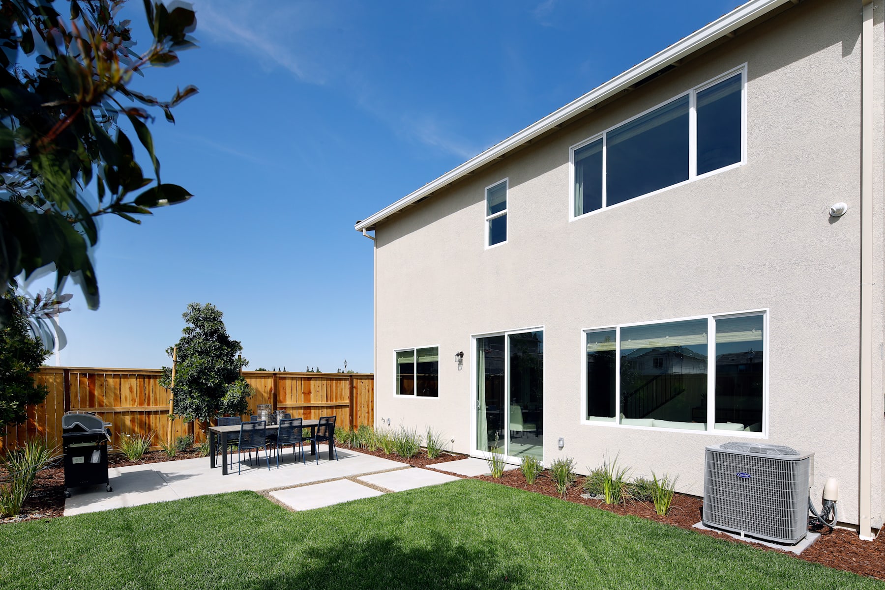 A modern two-story house with a well-maintained yard, featuring a patio area with outdoor furniture and a lush green lawn in the foreground.