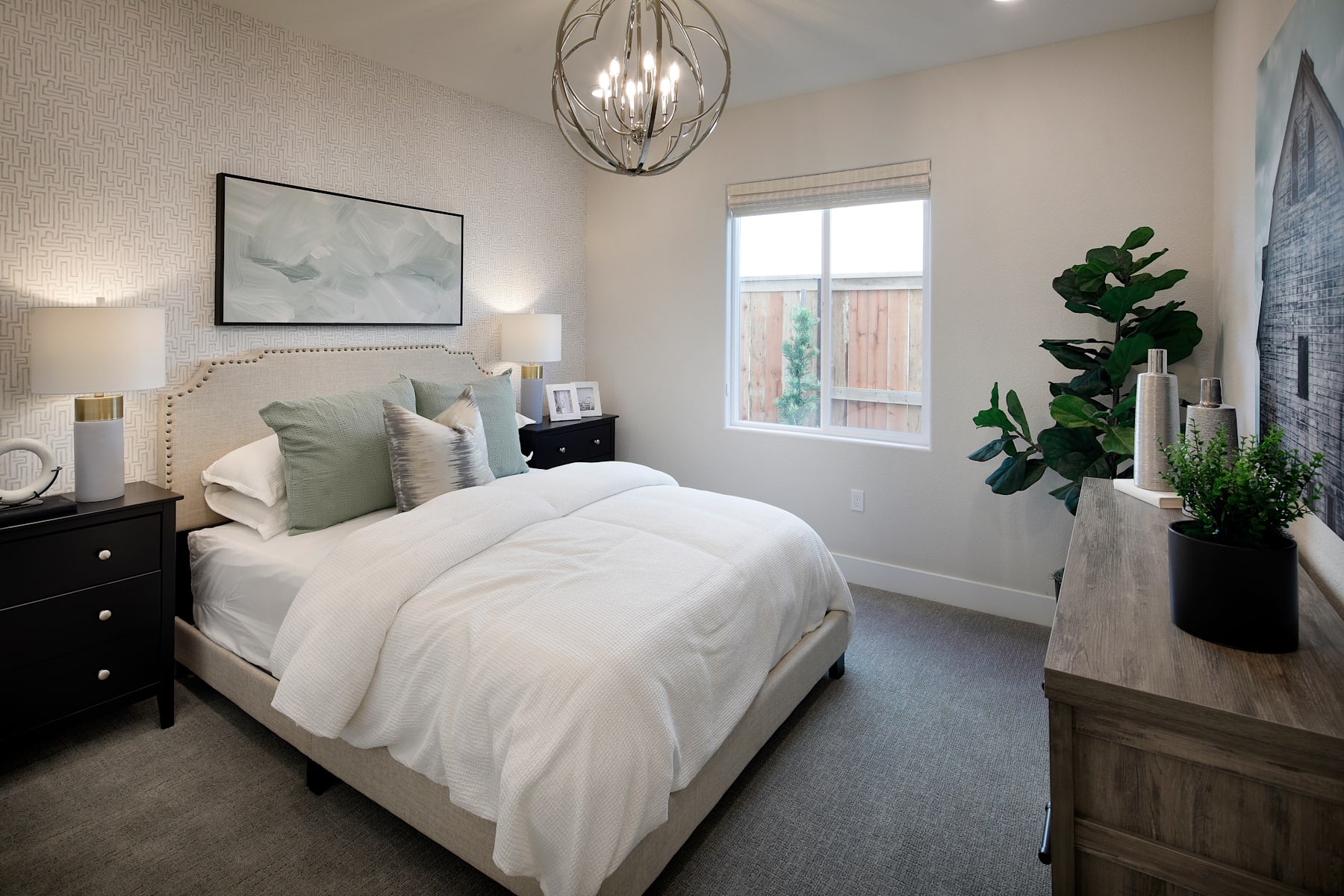 A cozy and well-decorated bedroom with a large bed, a modern chandelier, and a potted plant adding a touch of greenery to the space.