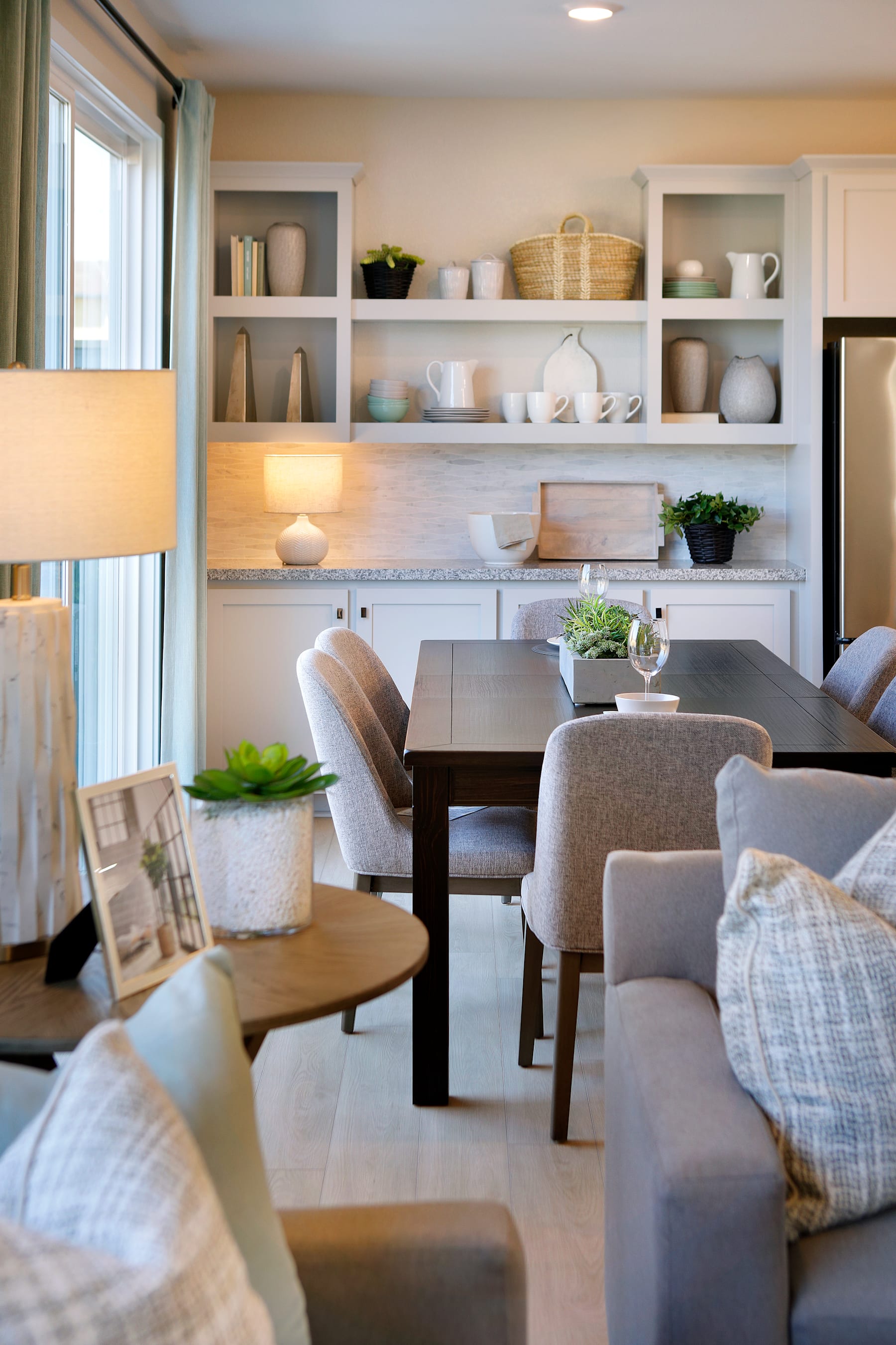 A cozy and inviting dining area with a wooden table, plush gray chairs, and open shelving displaying an array of decorative items and plants, creating a warm and welcoming atmosphere.