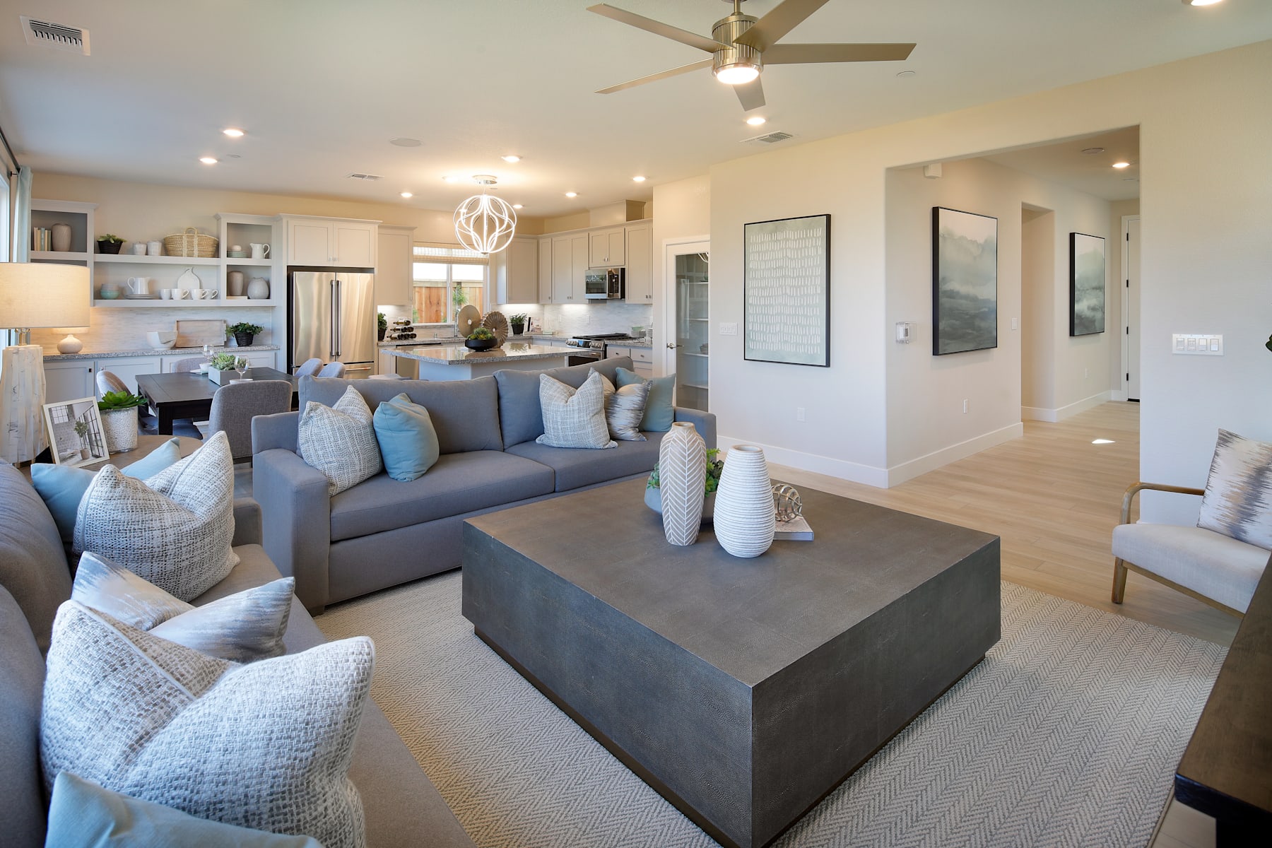 A modern and stylish living room with a gray sectional sofa, a large coffee table, and various decorative elements such as artwork and shelving units in the background.