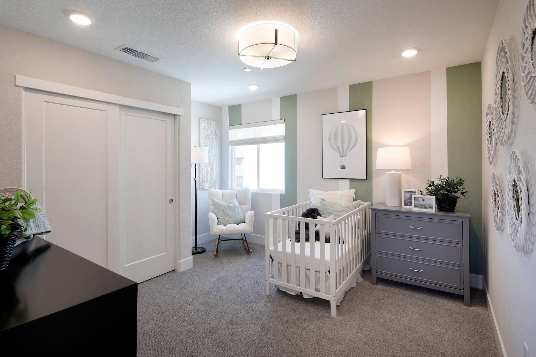 A cozy and well-designed nursery with a white crib, dresser, and a modern light fixture, set against a neutral color palette and accented with decorative elements.