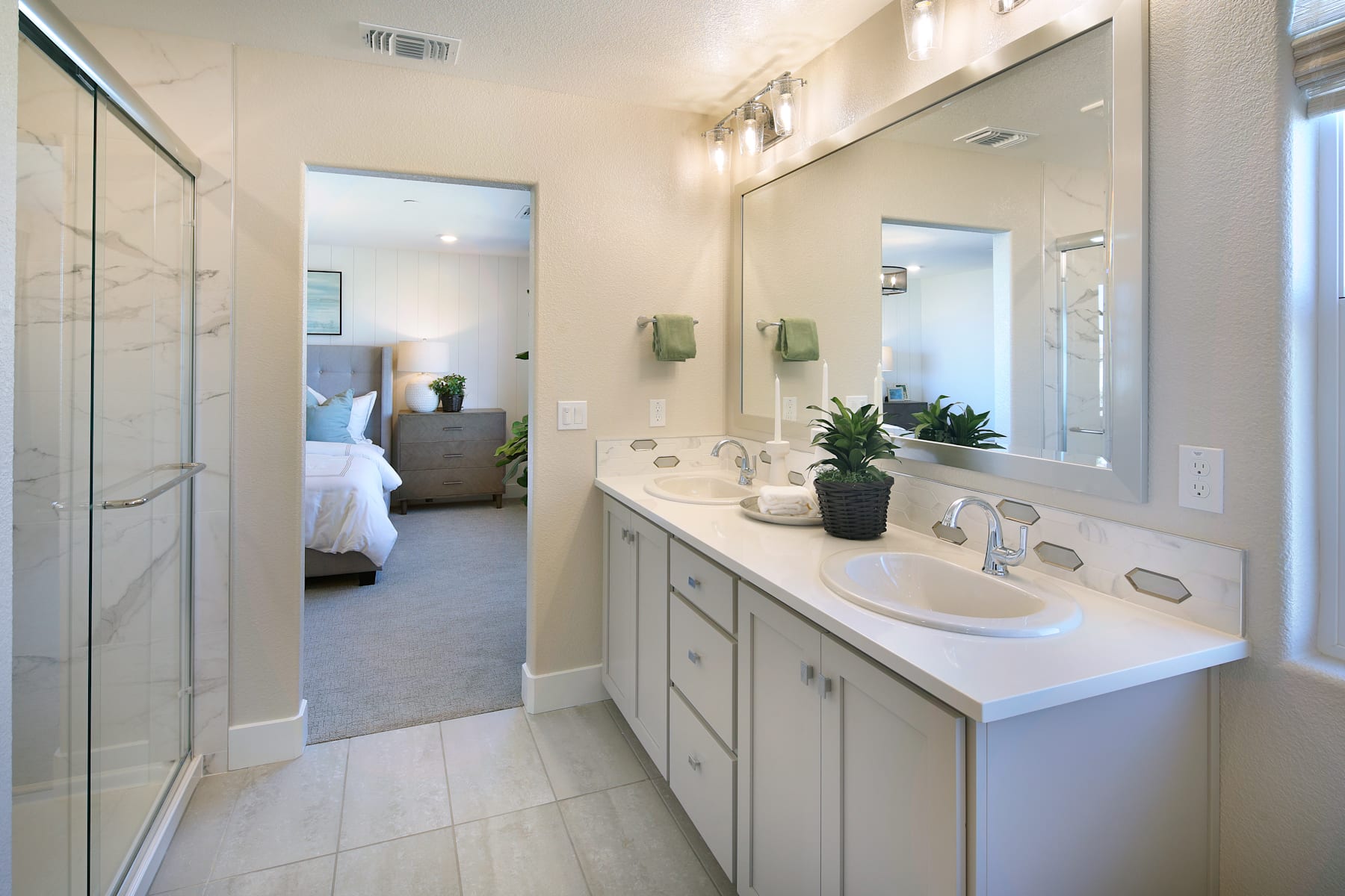 A modern and well-designed bathroom with a vanity, mirror, and a view of the bedroom in the background.