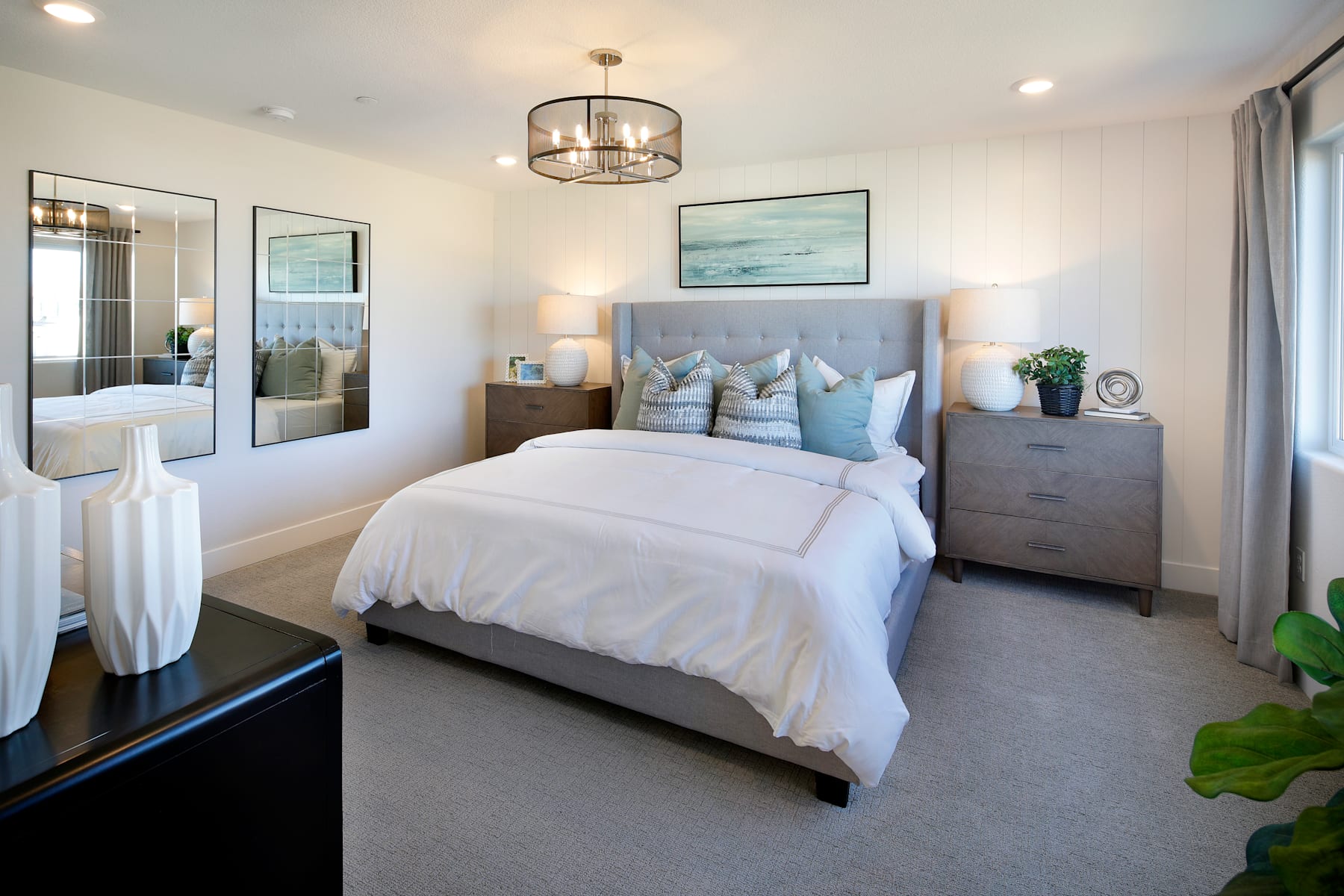A cozy and inviting bedroom with a plush bed, decorative pillows, and a large framed artwork on the wall, complemented by a stylish chandelier and a potted plant in the corner.