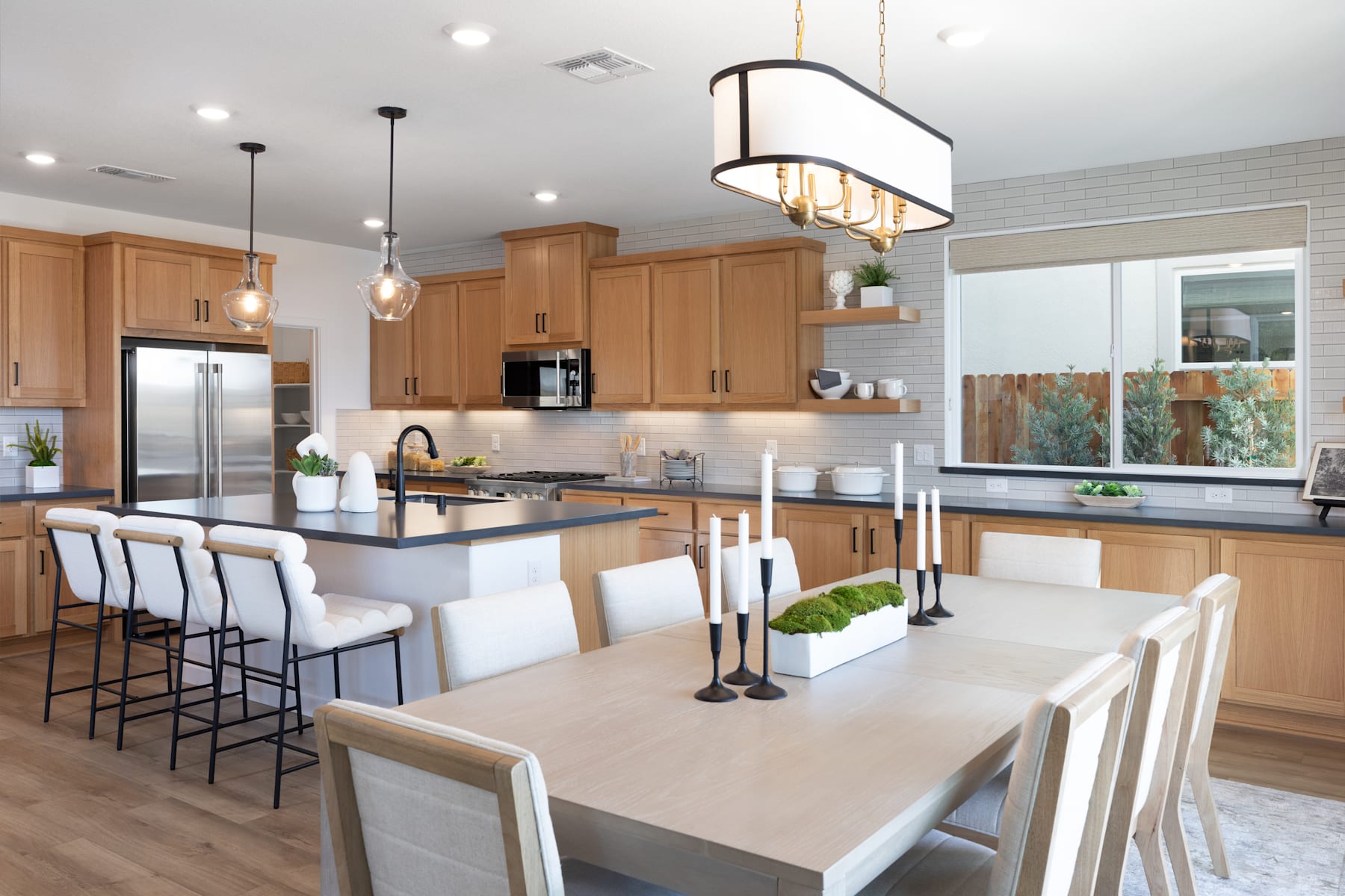 A modern and spacious kitchen with wooden cabinets, a large dining table, and a central island with bar stools, all illuminated by a stylish pendant light fixture.
