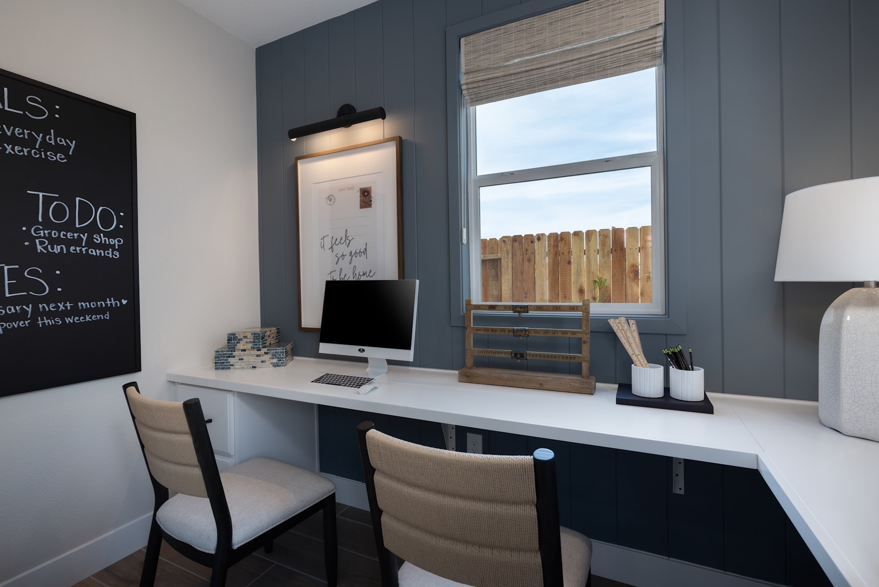 A cozy home office space with a white desk, wooden shelves, and a chalkboard wall displaying a to-do list.