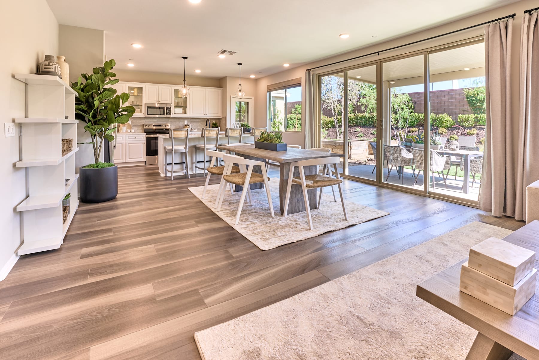 A spacious and modern open-plan kitchen and dining area with wooden floors, large windows overlooking a backyard, and a mix of contemporary and natural elements in the decor.