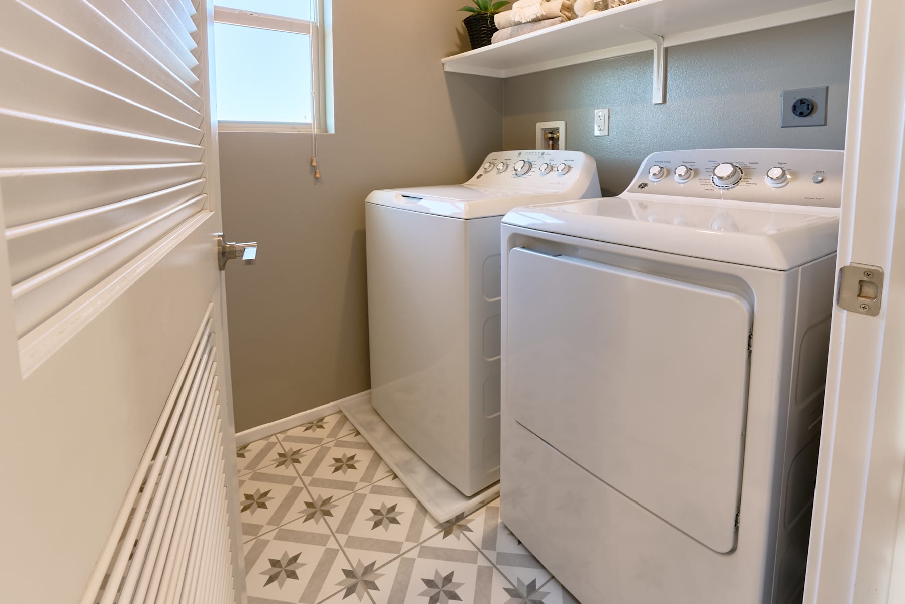 A small laundry room with a washer and dryer, shelves, and a patterned tile floor.