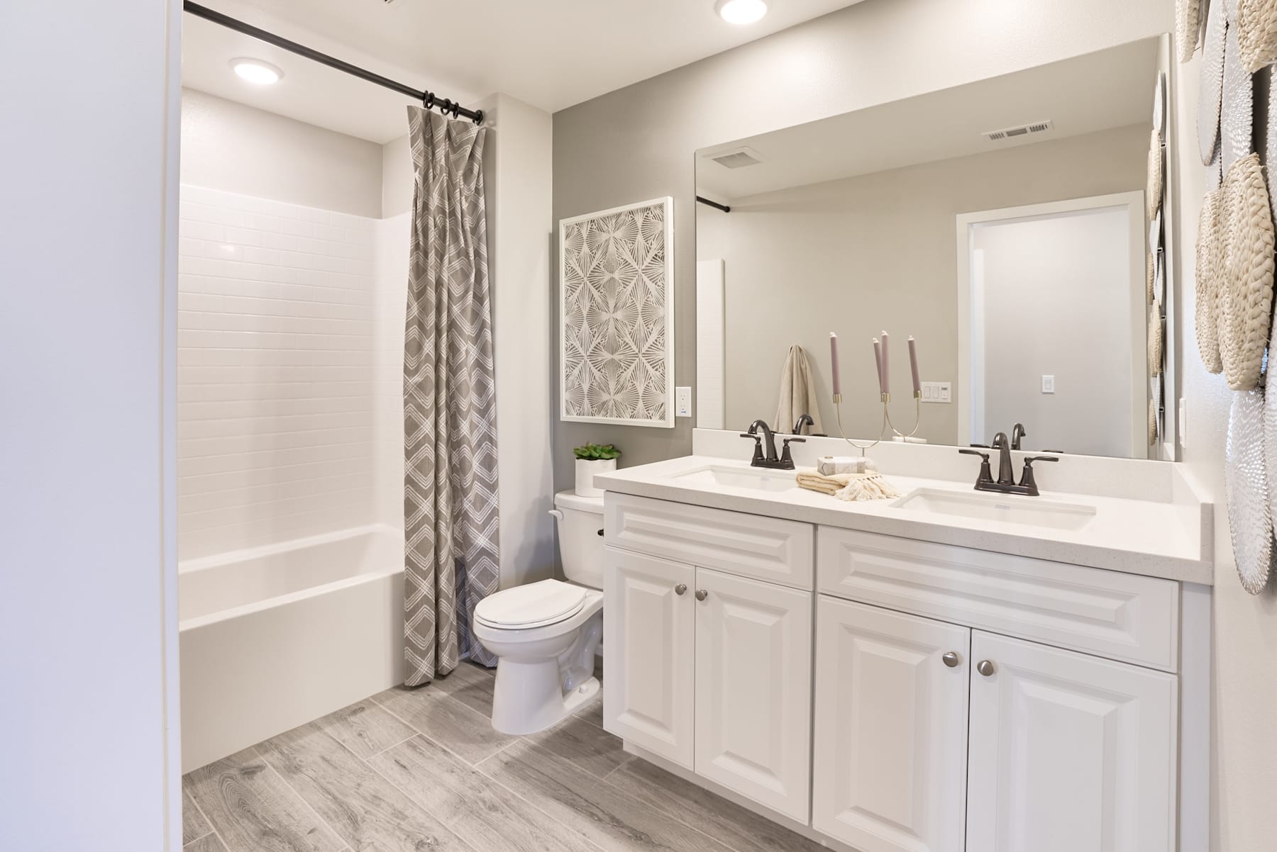 A modern and well-designed bathroom with white cabinets, a vanity with dual sinks, and a shower curtain with a patterned design. The floor appears to be made of light-colored wood-like tiles, creating a clean and cohesive look.