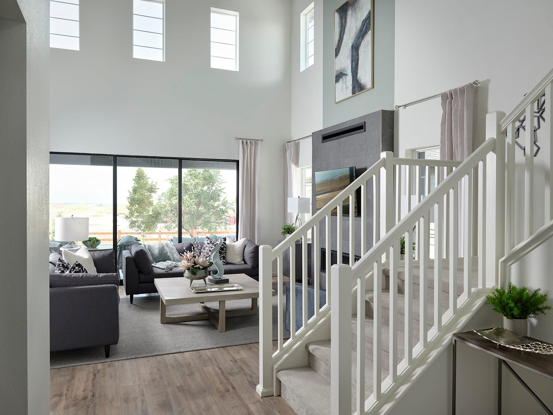A spacious and bright living room with a staircase leading to an upper level, featuring a cozy seating area with a gray sofa and a decorative plant on a side table.