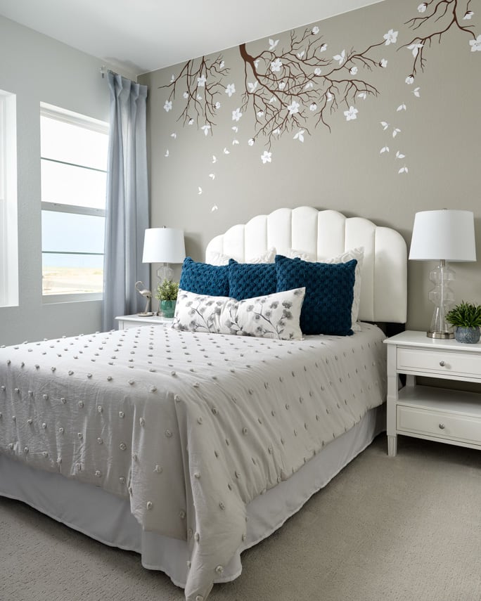 A cozy and serene bedroom with a plush white bed, patterned bedding, and a striking floral wall mural creating a calming and inviting atmosphere.
