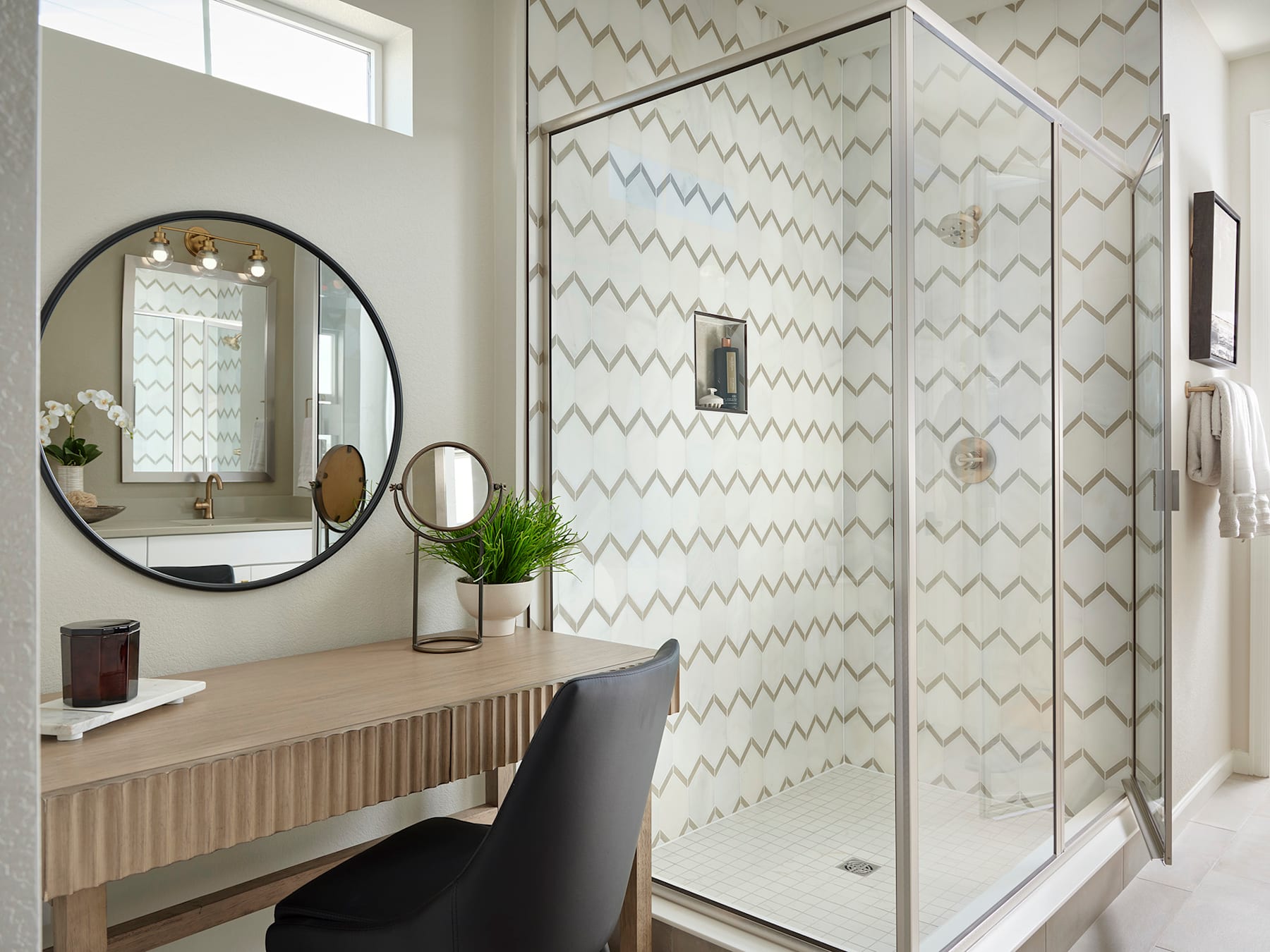 A modern bathroom with a large circular mirror, a wooden vanity, and a glass-enclosed shower with a patterned tile wall.