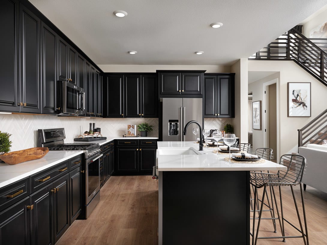 A modern and sleek kitchen with dark cabinets, white countertops, and stainless steel appliances, complemented by a central island and bar stools.