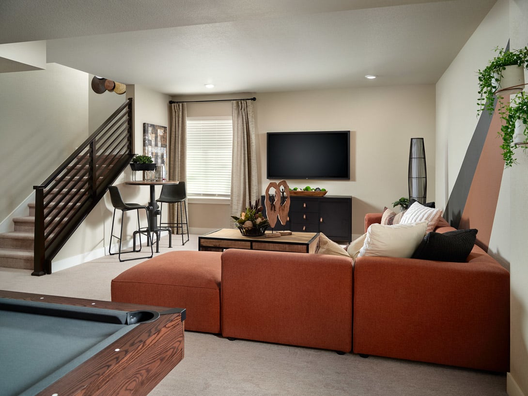 A cozy and inviting living room with a large orange sectional sofa, a TV mounted on the wall, and various decorative elements such as plants and artwork, creating a warm and comfortable atmosphere.