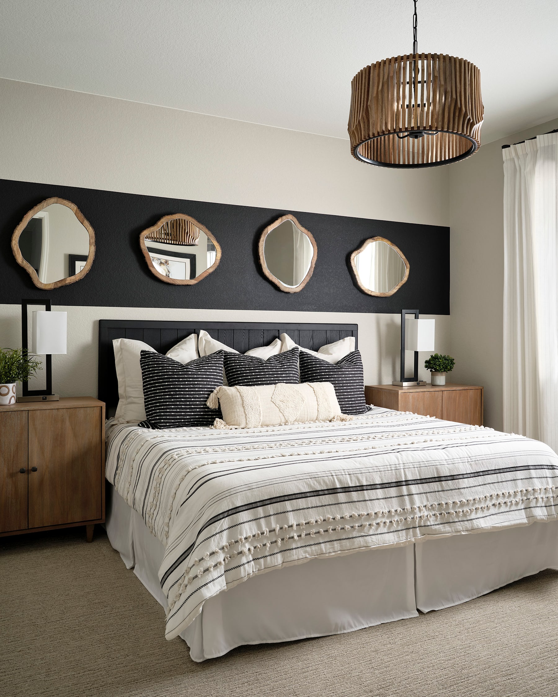 A cozy and stylish bedroom with a large bed, patterned bedding, and a collection of decorative mirrors on the wall, illuminated by a modern pendant light fixture.