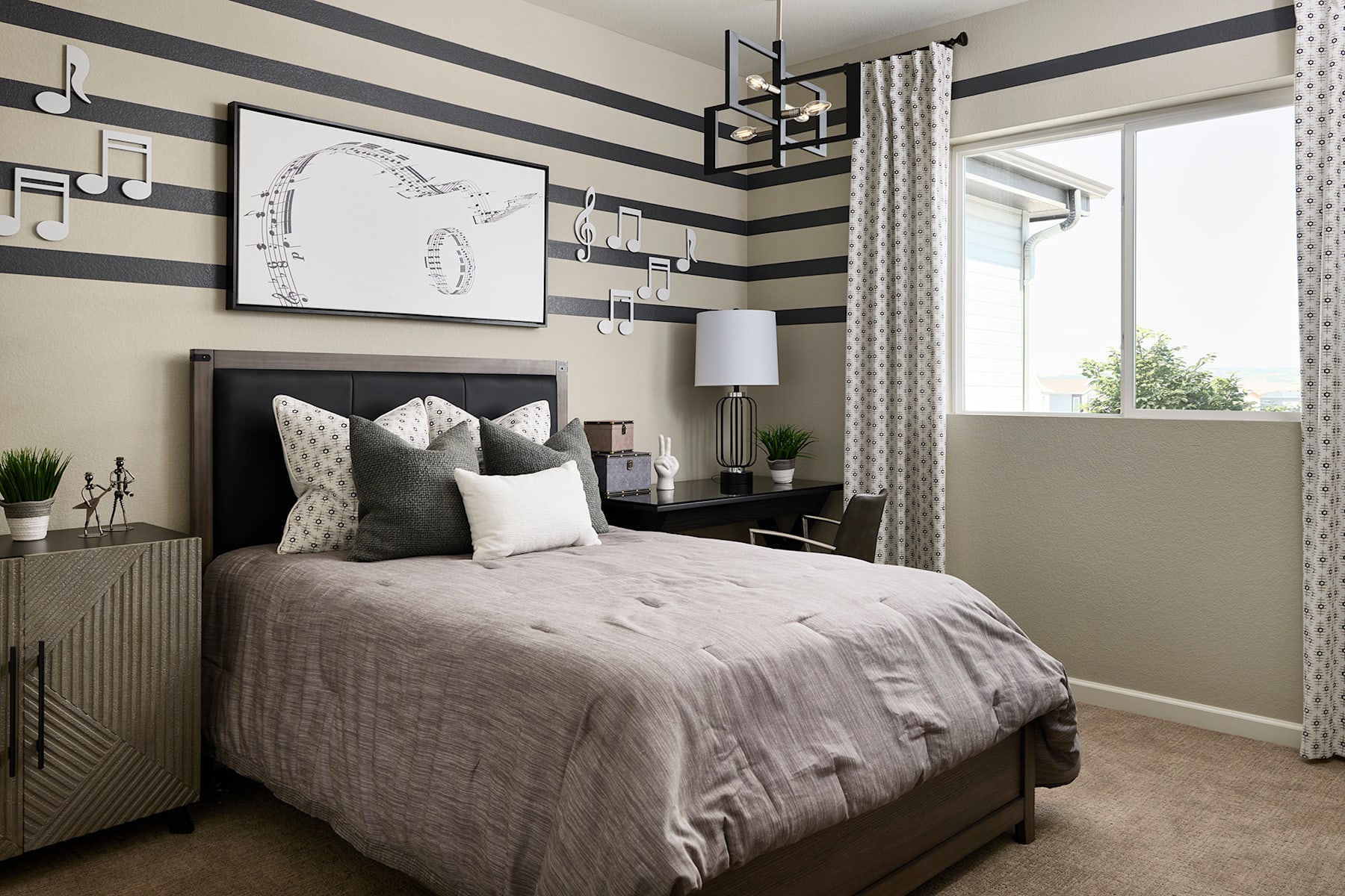 A cozy and stylish bedroom with a black and white striped accent wall, a plush gray bedding set, and various decorative elements such as artwork, lamps, and potted plants.