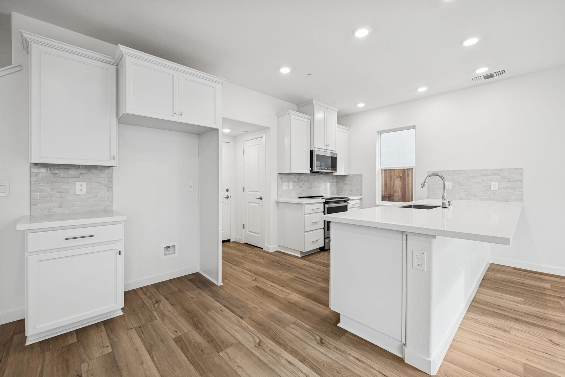 A modern, bright, and spacious kitchen with white cabinets, a marble-like countertop, and hardwood floors.