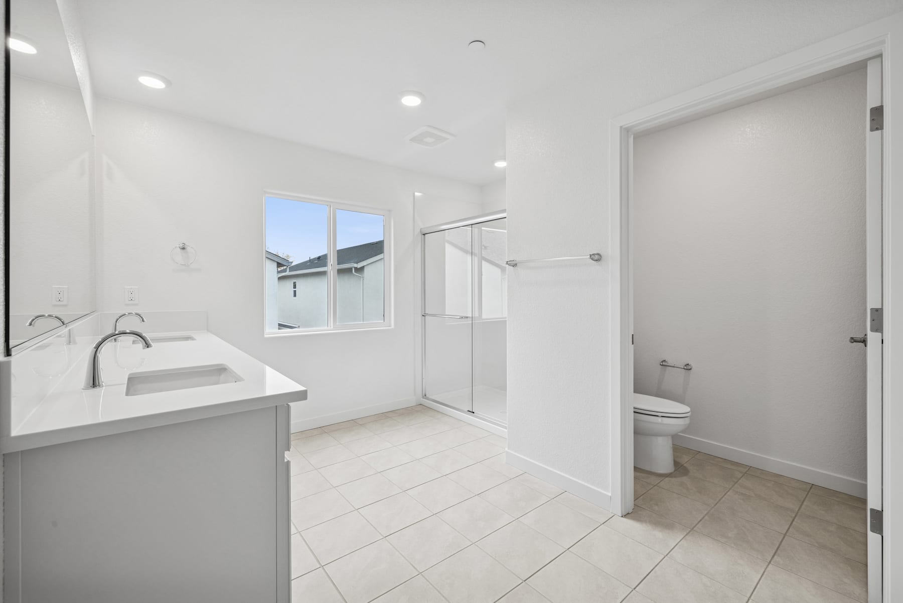 A modern, minimalist bathroom with a vanity, toilet, and glass-enclosed shower area, all in a clean, white color scheme.
