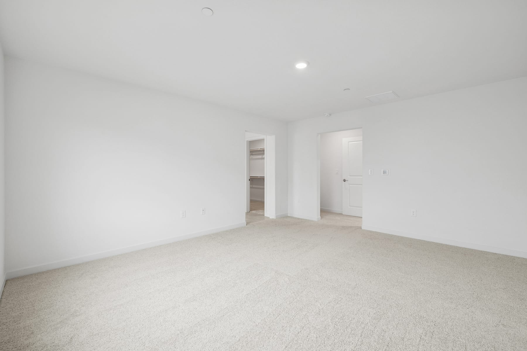 A spacious, empty room with white walls and a carpeted floor, illuminated by a single light source.